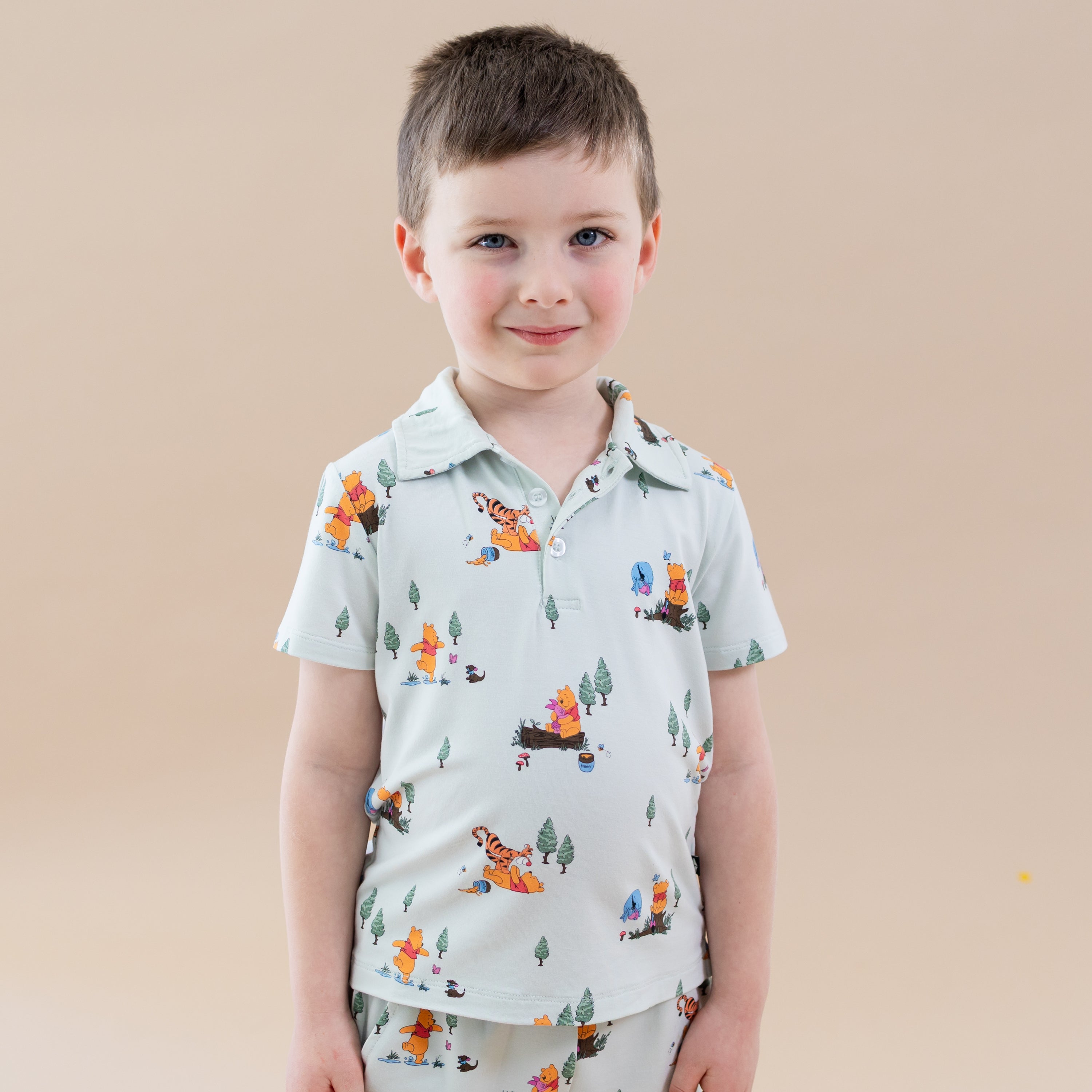 Young boy wearing the Toddler Short Sleeve Polo in Winnie the Pooh Hundred Acre Wood paired with matching shorts