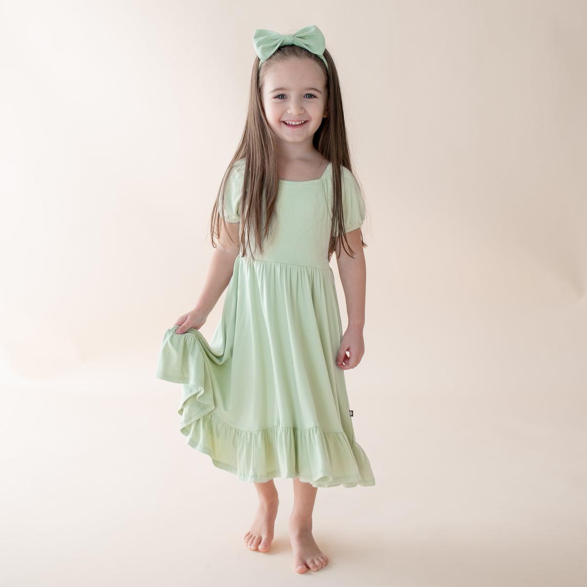 Young girl wearing a light green dress with a bow in her hair on a plain background