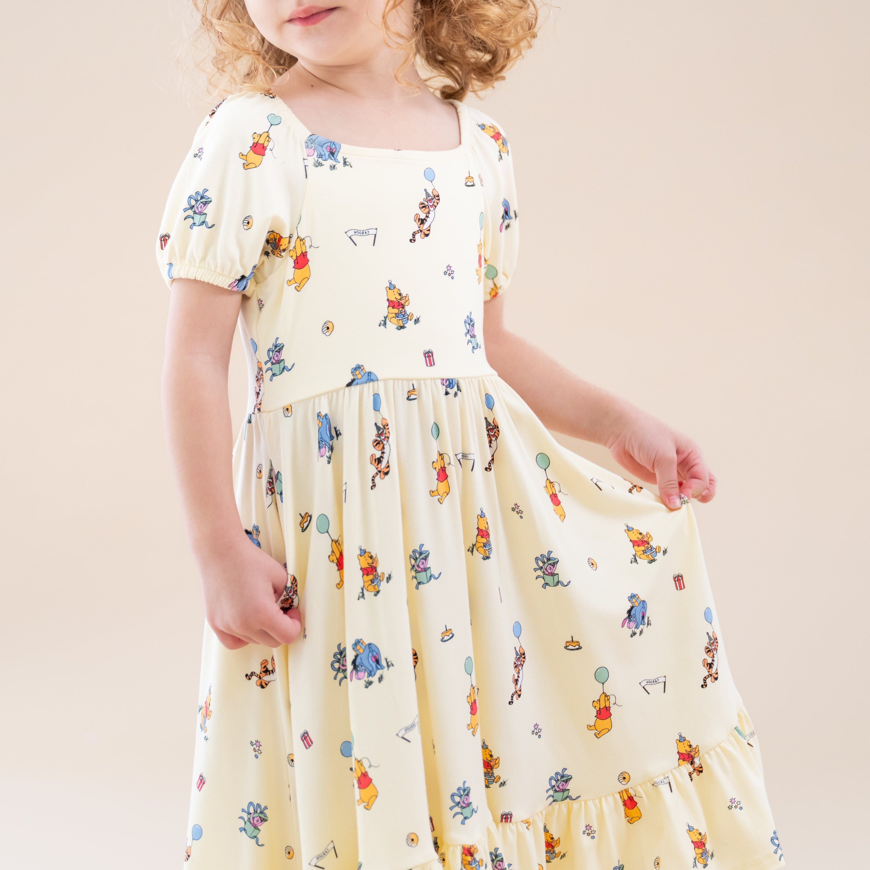 Close up of the Puff Sleeve Twirl Dress in Winnie the Pooh Celebration shown on a young girl