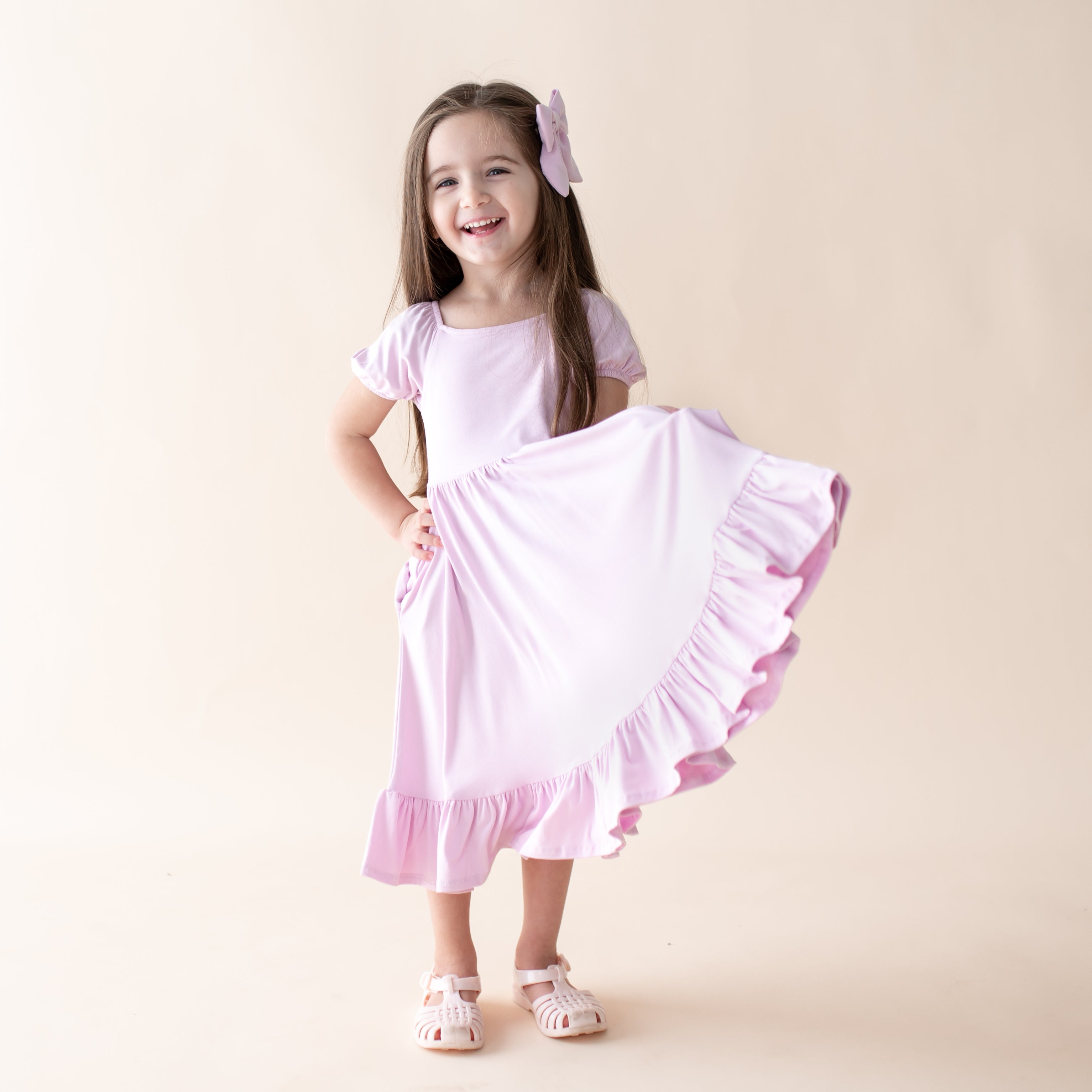 Young girl wearing a light purple dress with ruffled skirt on a beige background