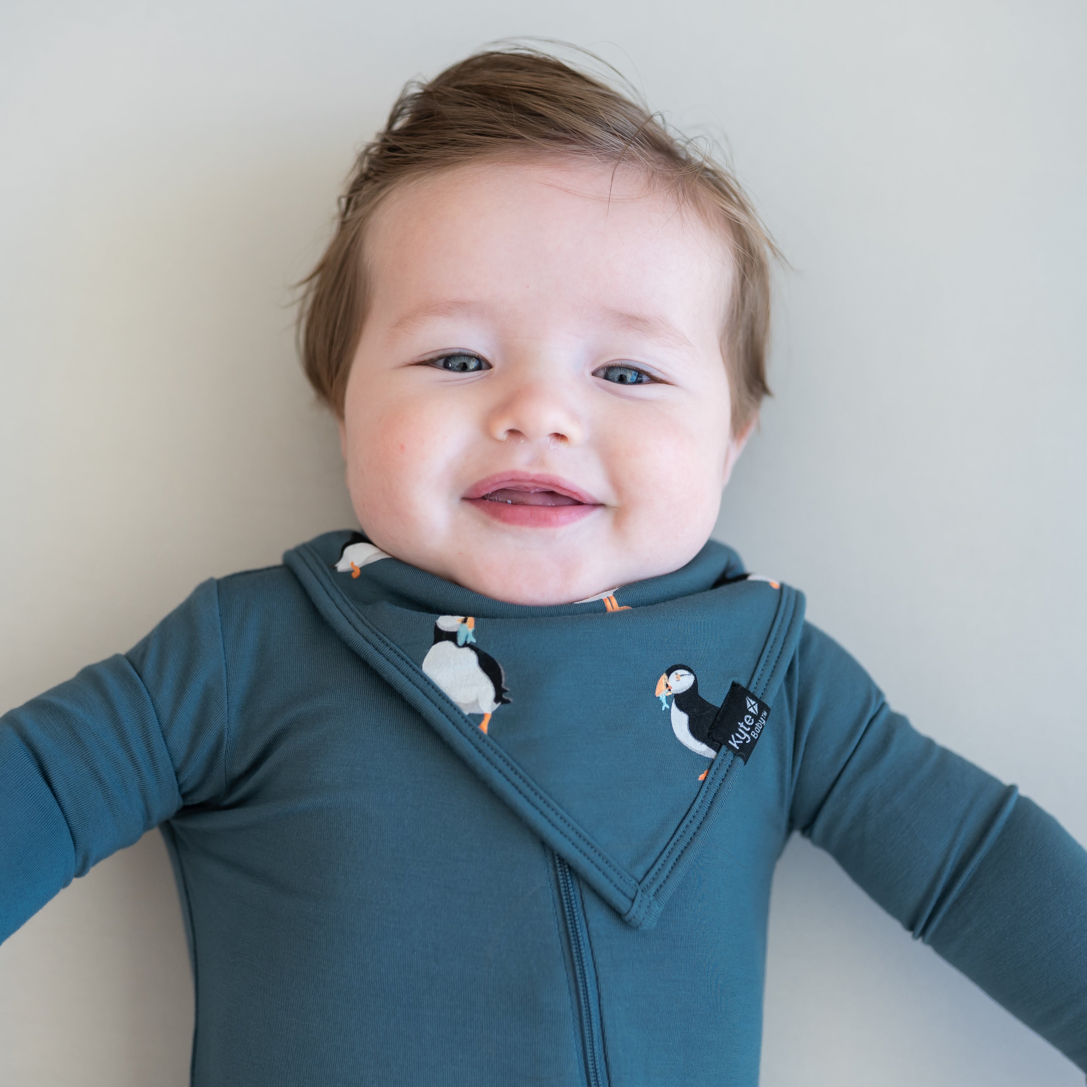 Close up of baby wearing the Bib in Puffin overtop an Atlantic zippered romper