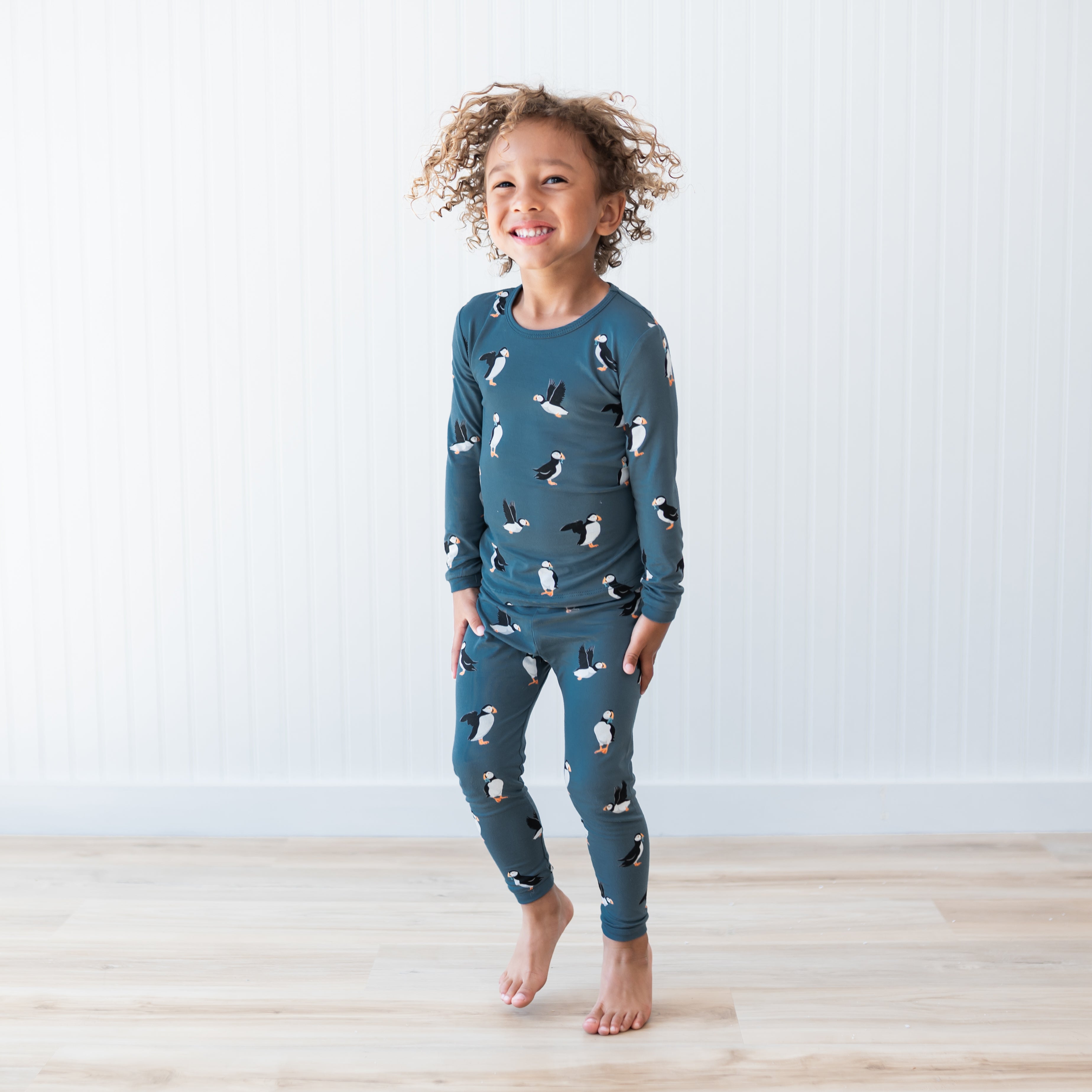 Young child jumping wearing the Long Sleeve Pajamas in Puffin in front of a white paneled wall