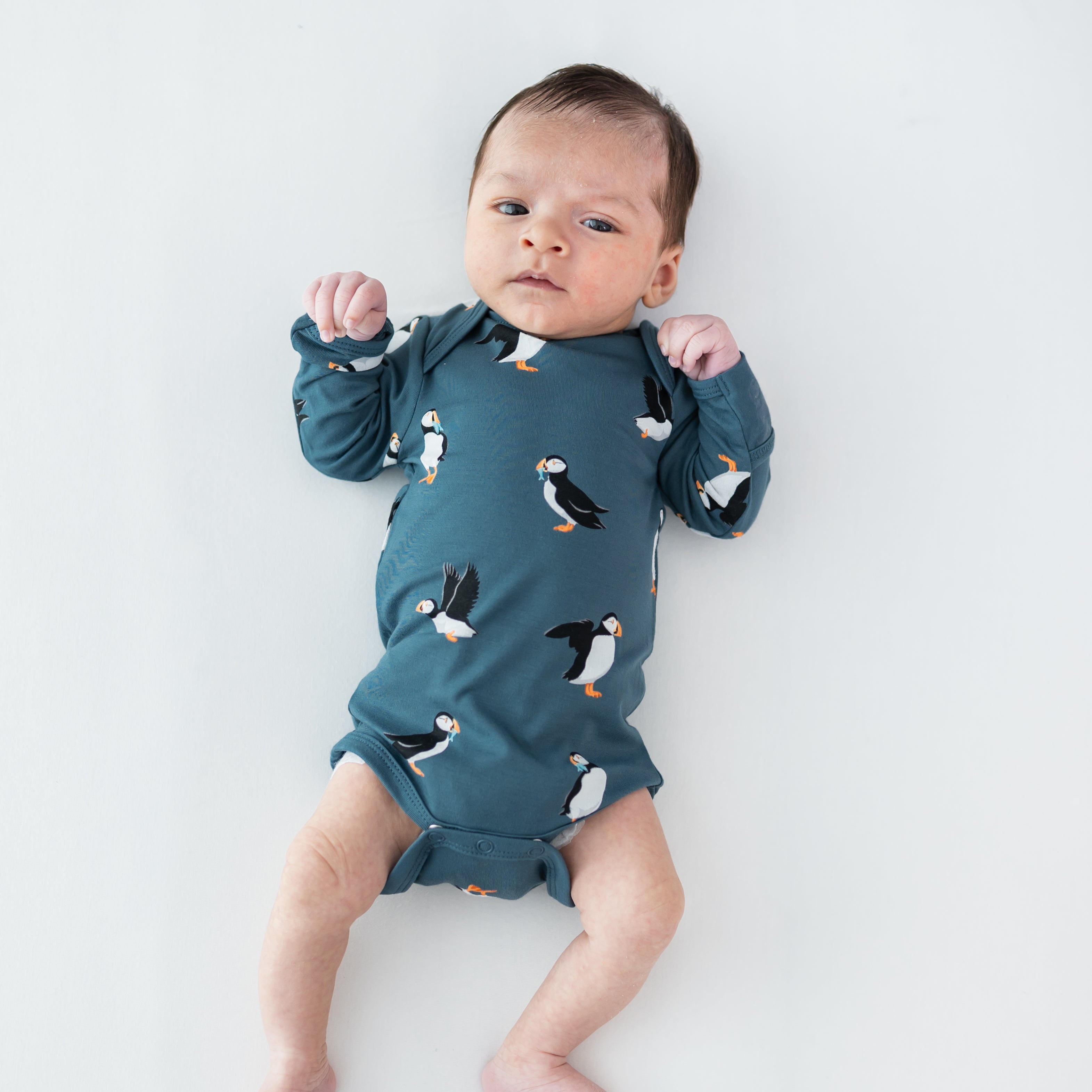 Infant wearing the Long Sleeve Bodysuit in Puffin laying on a light neutral surface