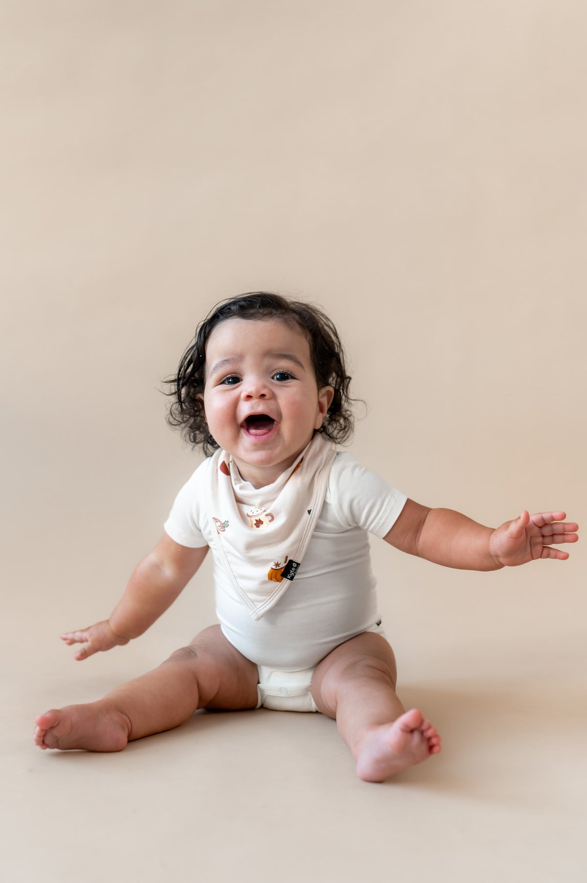 Baby wearing Bib with Pumpkin Spice Latte over white bodysuit on a beige background