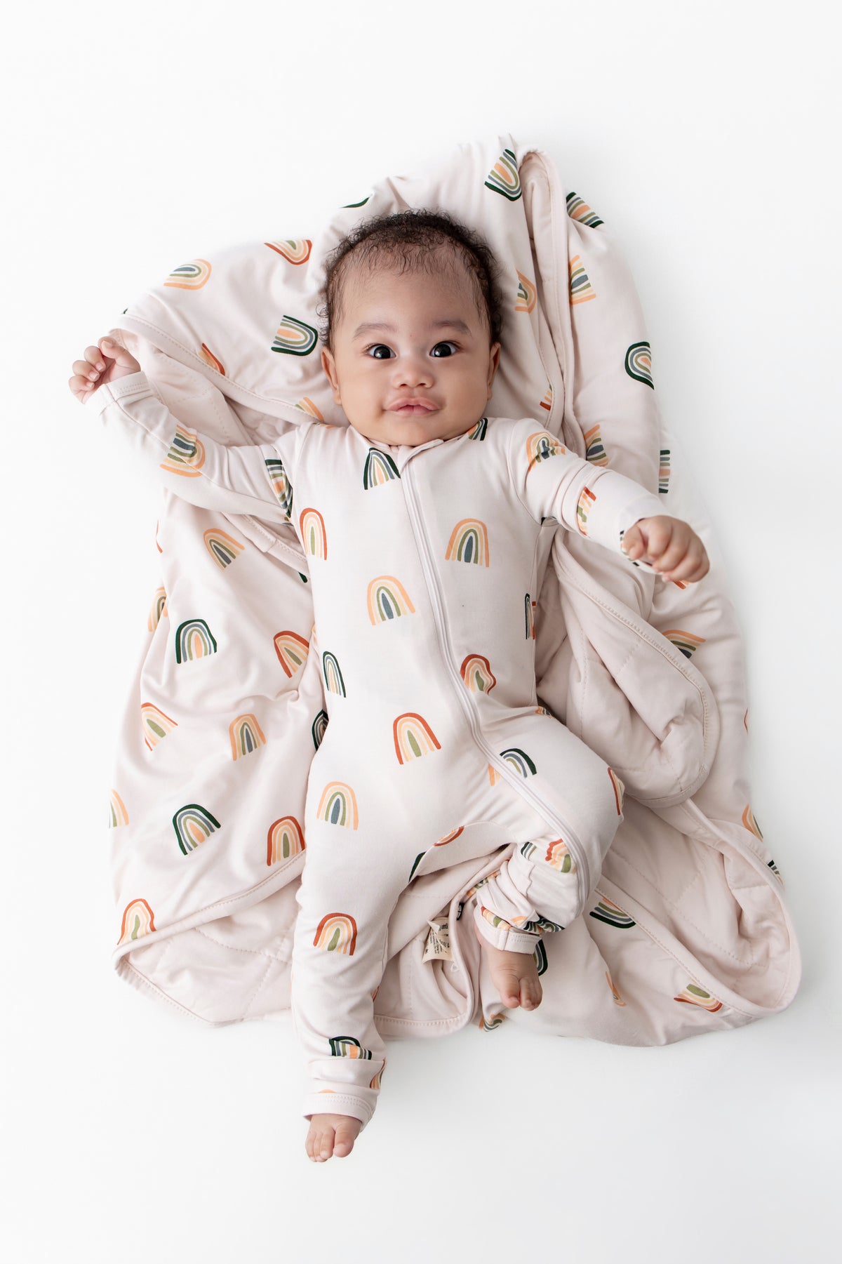 Baby lying on Baby Blanket with Retro Rainbow print wearing similar print zippered romper on a white background