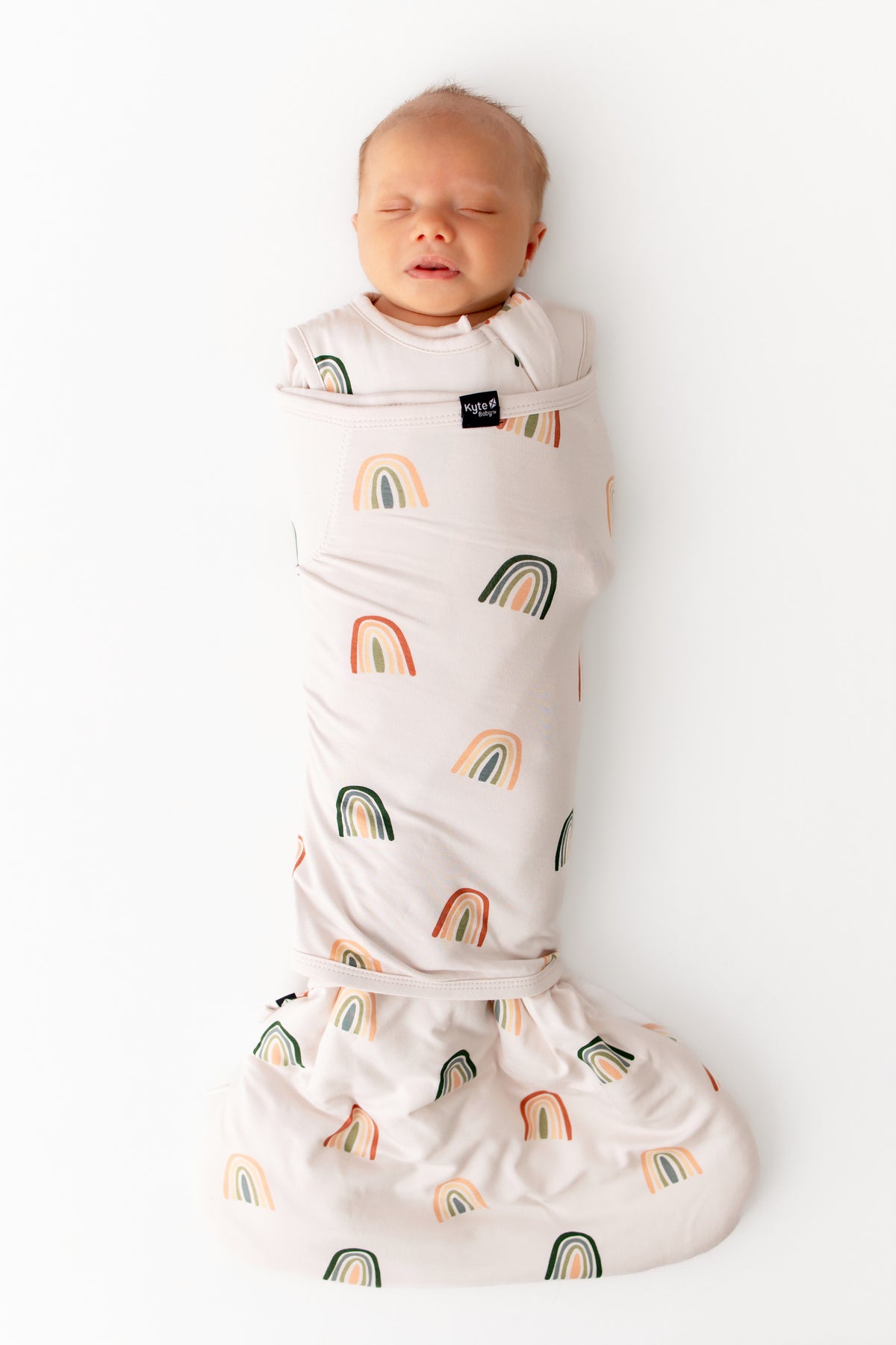Baby sleeping in Sleep Bag Swaddler in Retro Rainbow 1.0 print on a white background