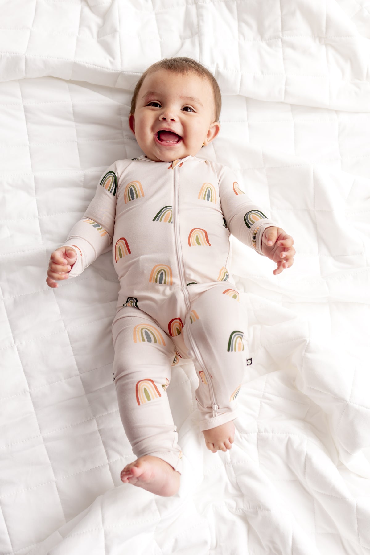 Baby posing in Zippered Romper in Retro Rainbow print on a white sheet