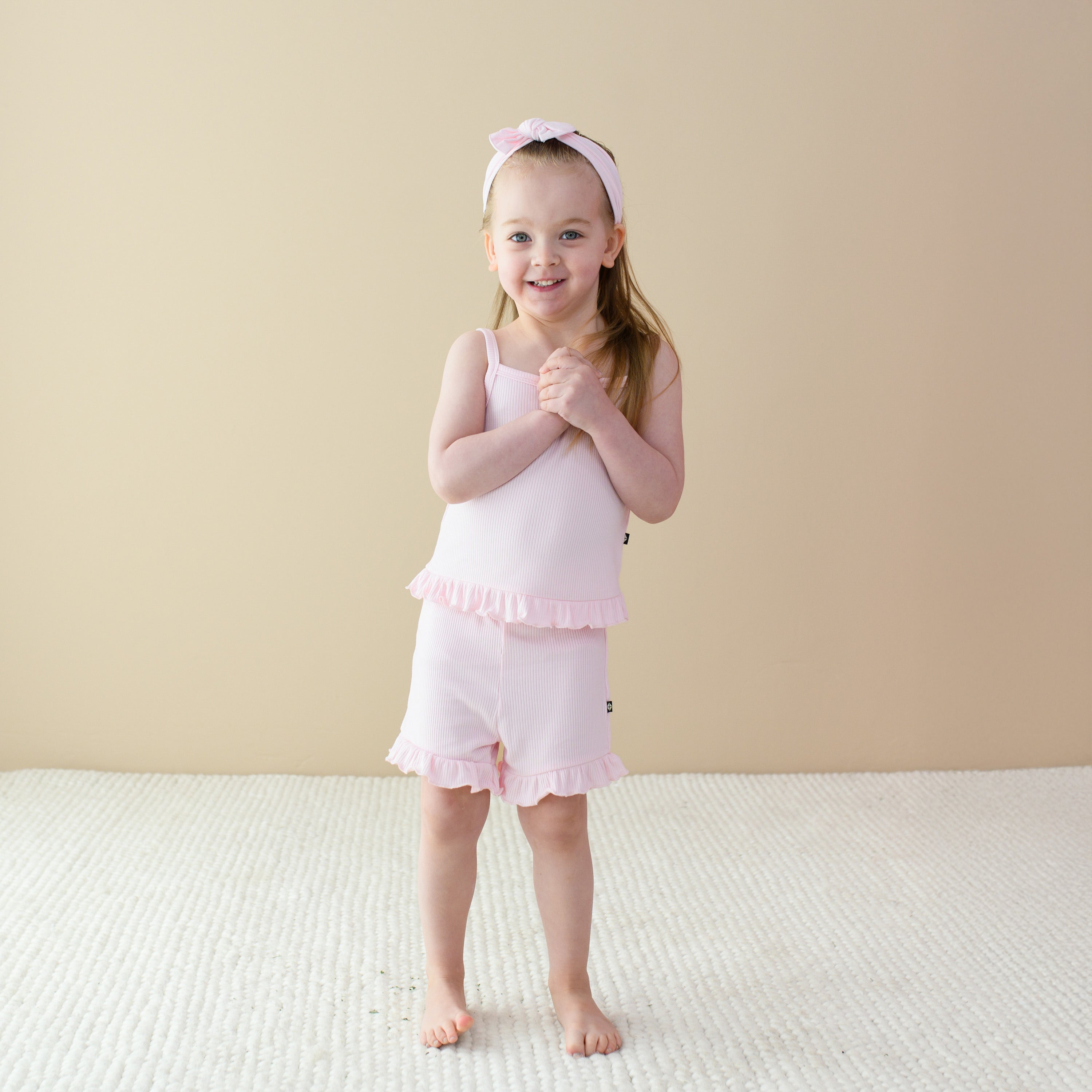 Girl wearing Bamboo Ribbed Ruffle Tank Set in Sakura with matching pink bow