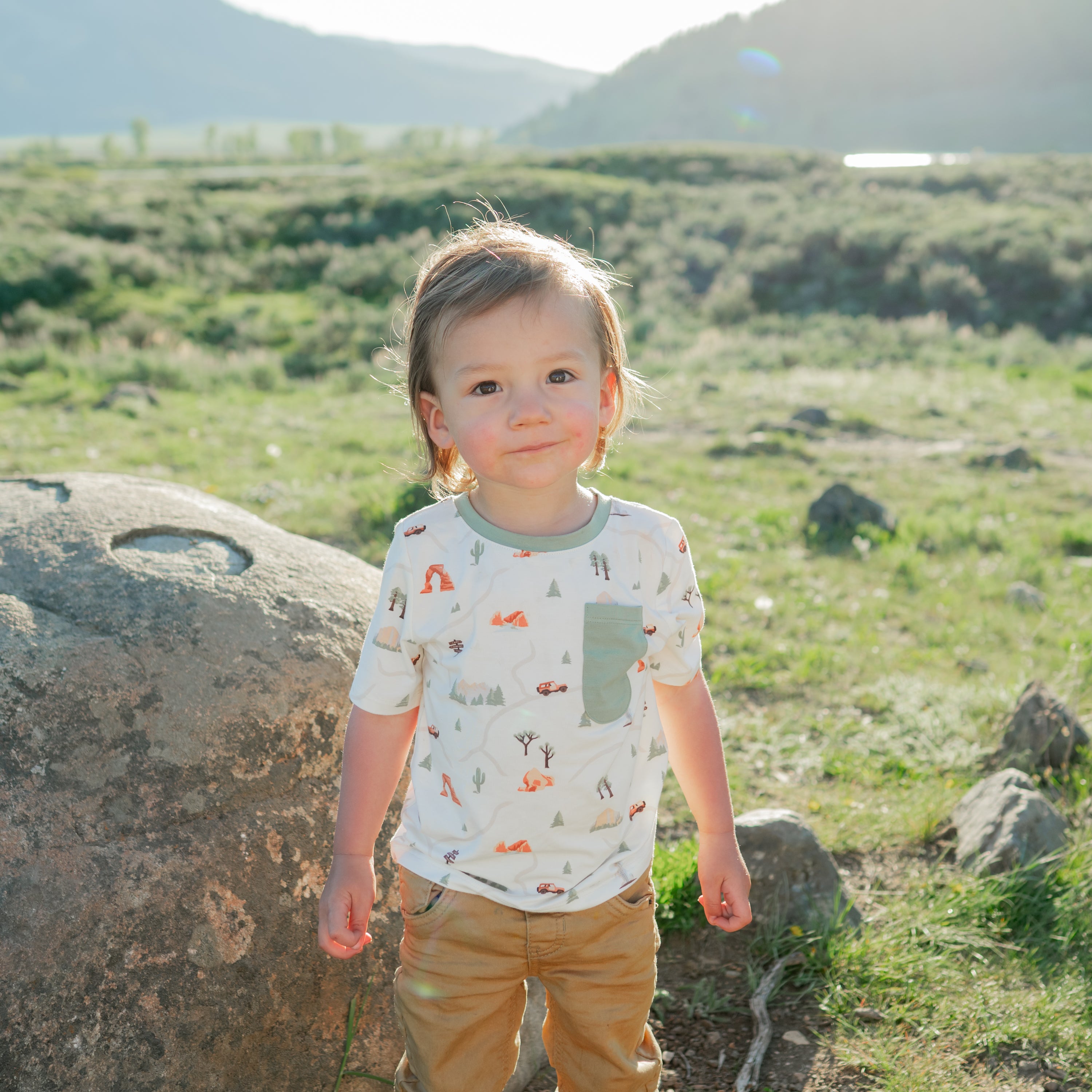 Toddler wearing the Toddler Crew Neck Tee in Road Trip paired with khaki pants standing in a field in a Montana National Park
