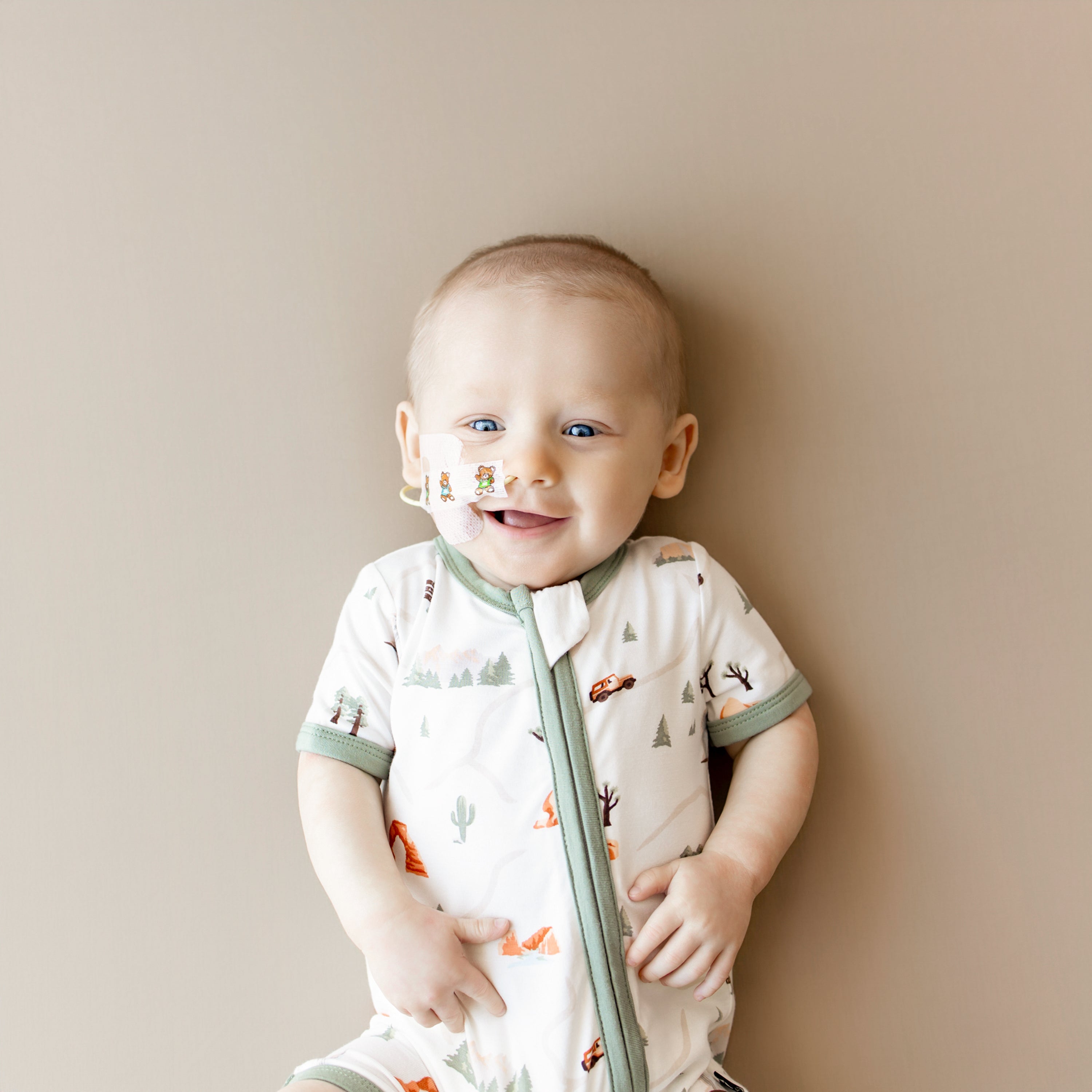 Close up of smiling infant wearing the Zippered Shortall Romper in Road Trip