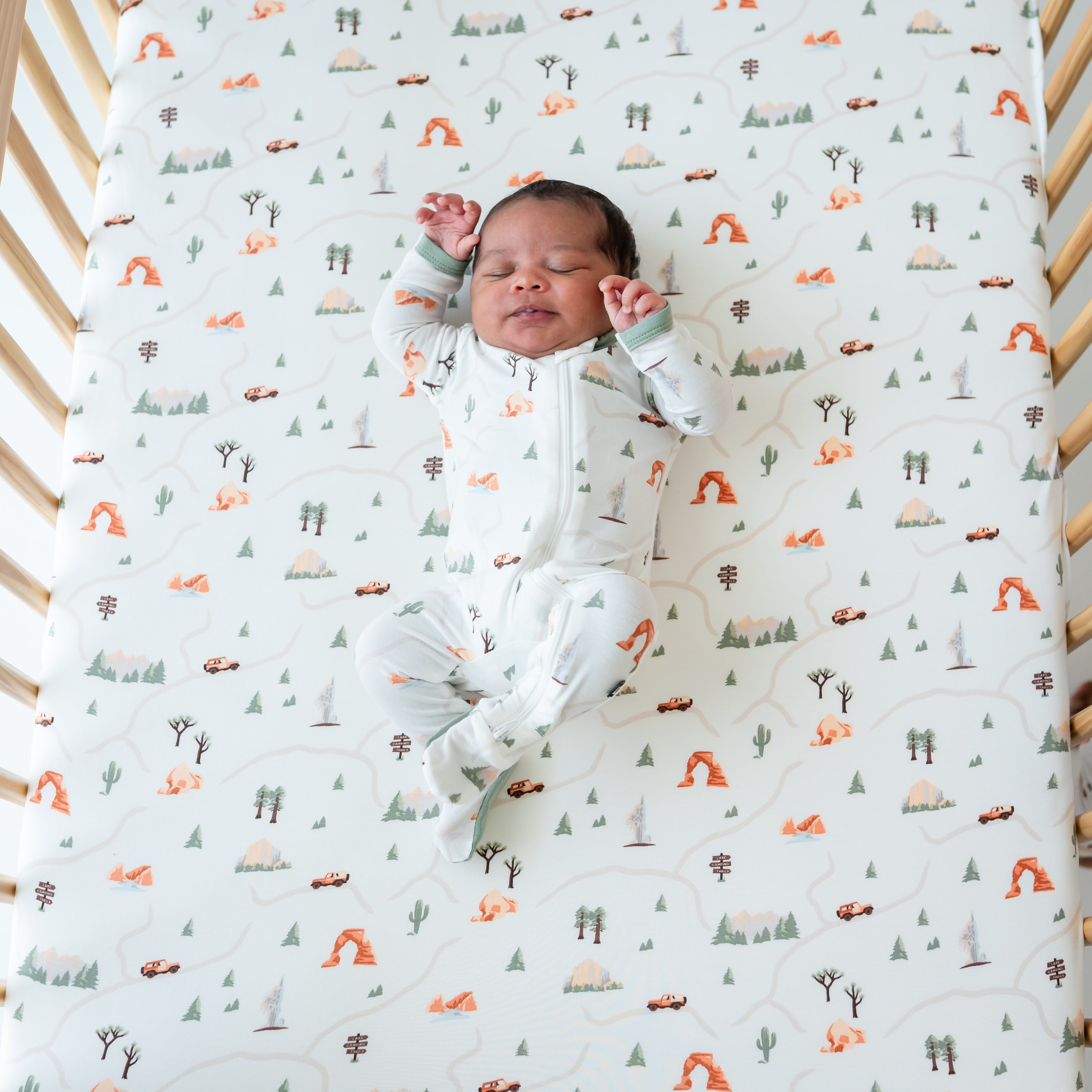 Newborn baby laying on Crib Sheet in Road Trip in a crib wearing a matching Zippered Footie