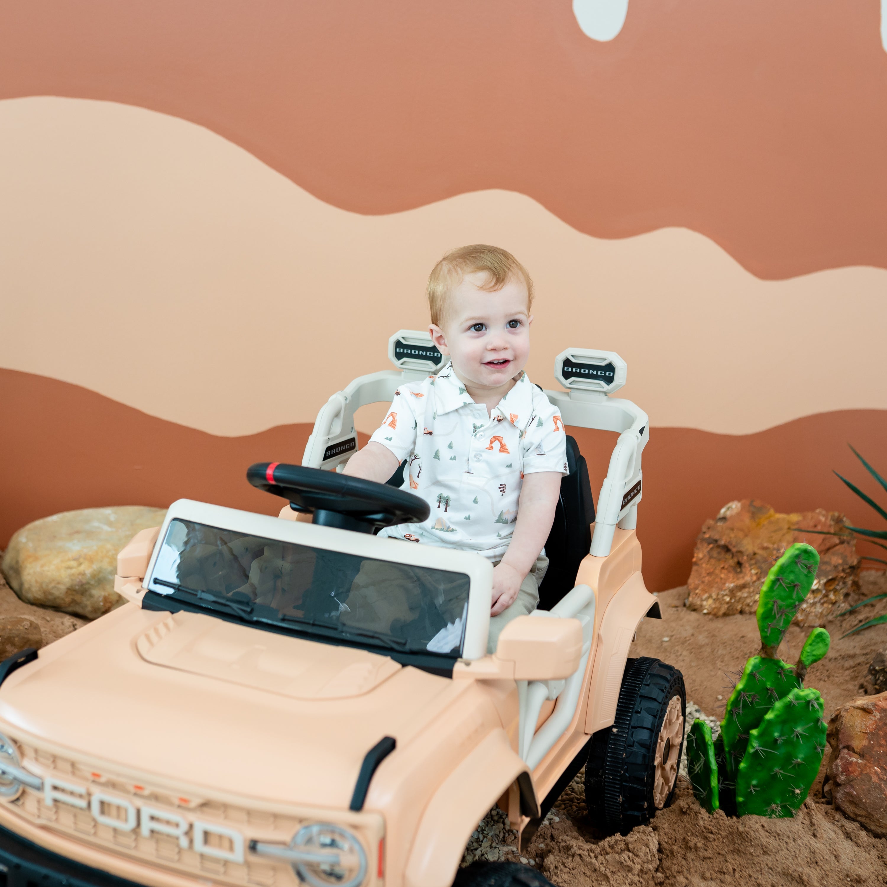 Toddler boy sitting in a Ford battery powered vehicle wearing the Toddler Short Sleeve Polo in Road Trip