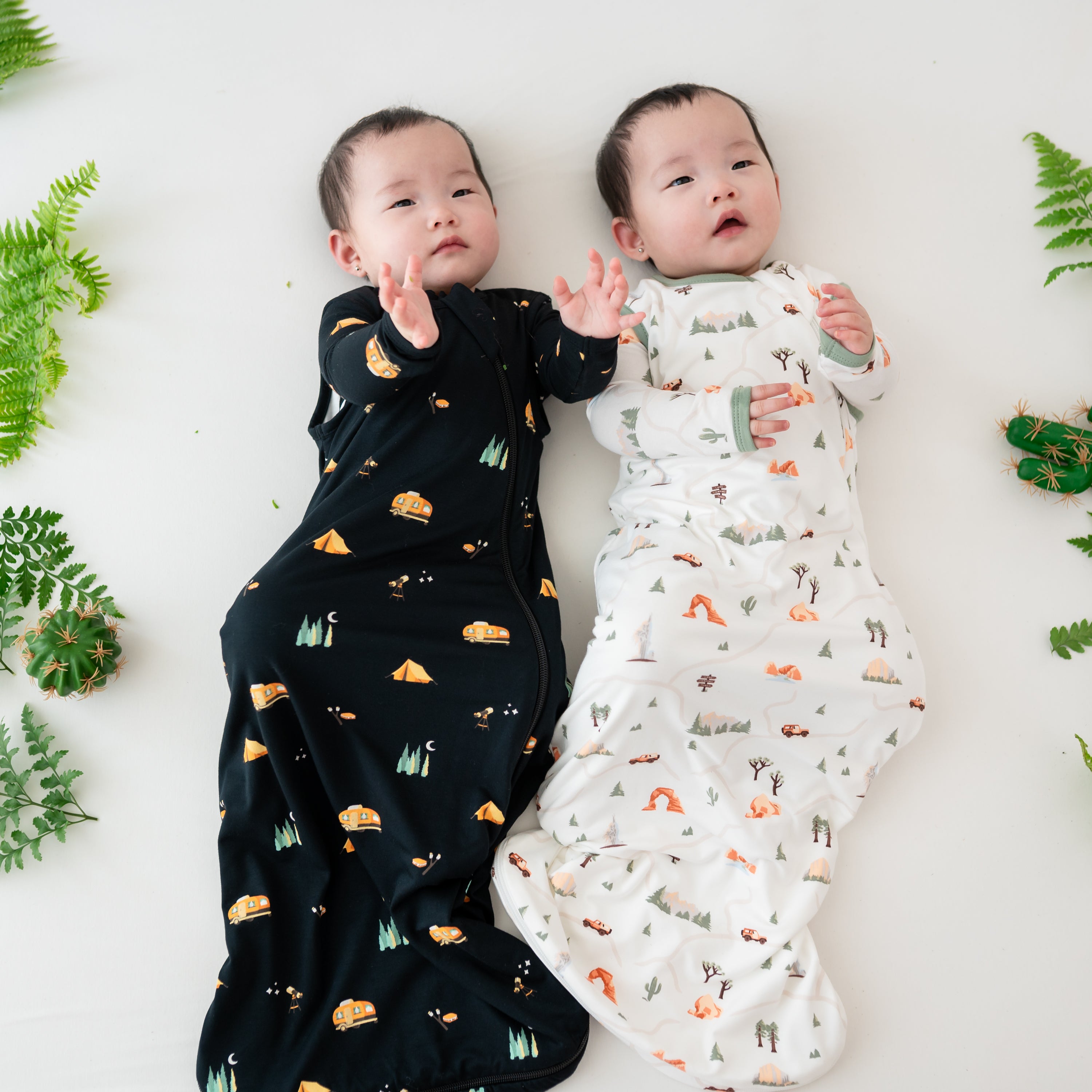 Twins laying next to eachother wearing the 0.5 TOG sleep bags in Under the Sun and Road Trip with matching long sleeve rompers