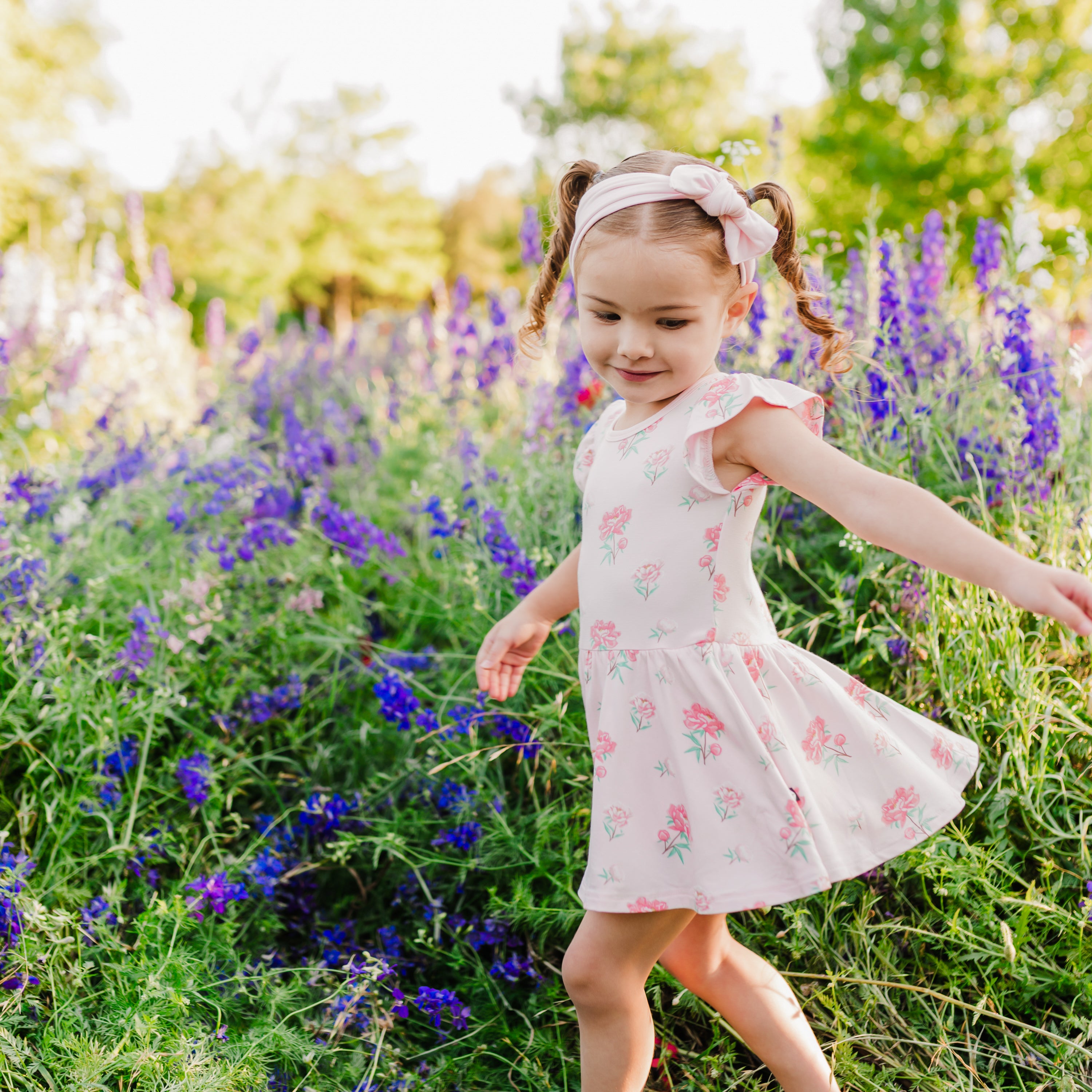 Toddler twirling in Twirl Bodysuit Dress in Sakura Peony with wildflower background