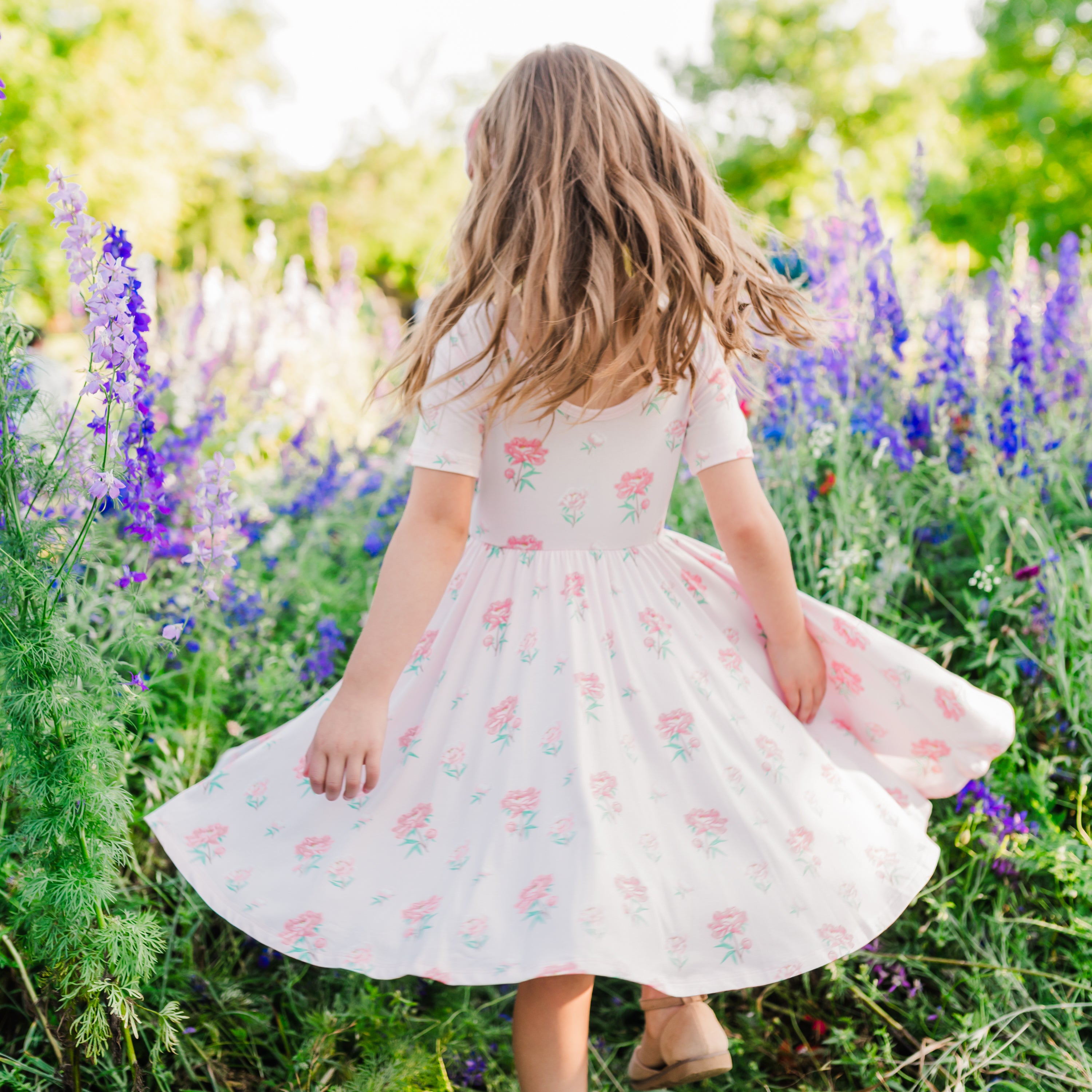 Child twirling in Twirl Dress in Sakura Peony with a wildflower field in background