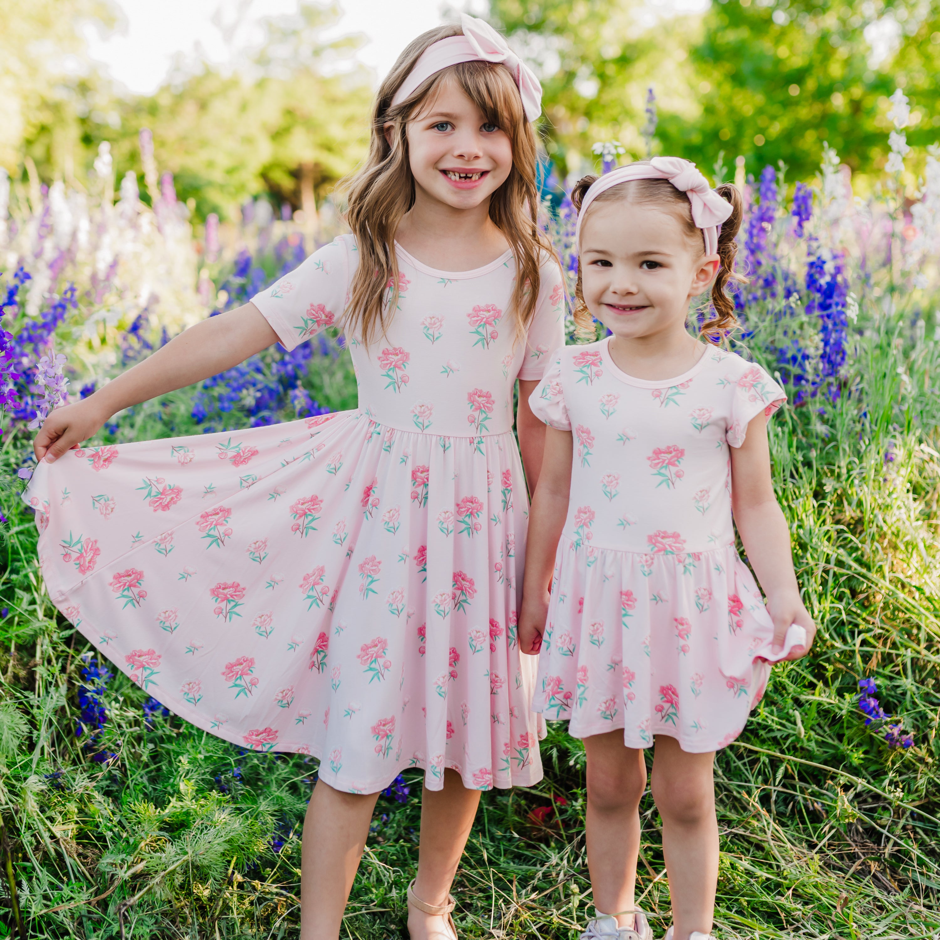Siblings modeling Twirl Dress and Twirl Bodysuit Dress in Sakura Peony with wildflower background