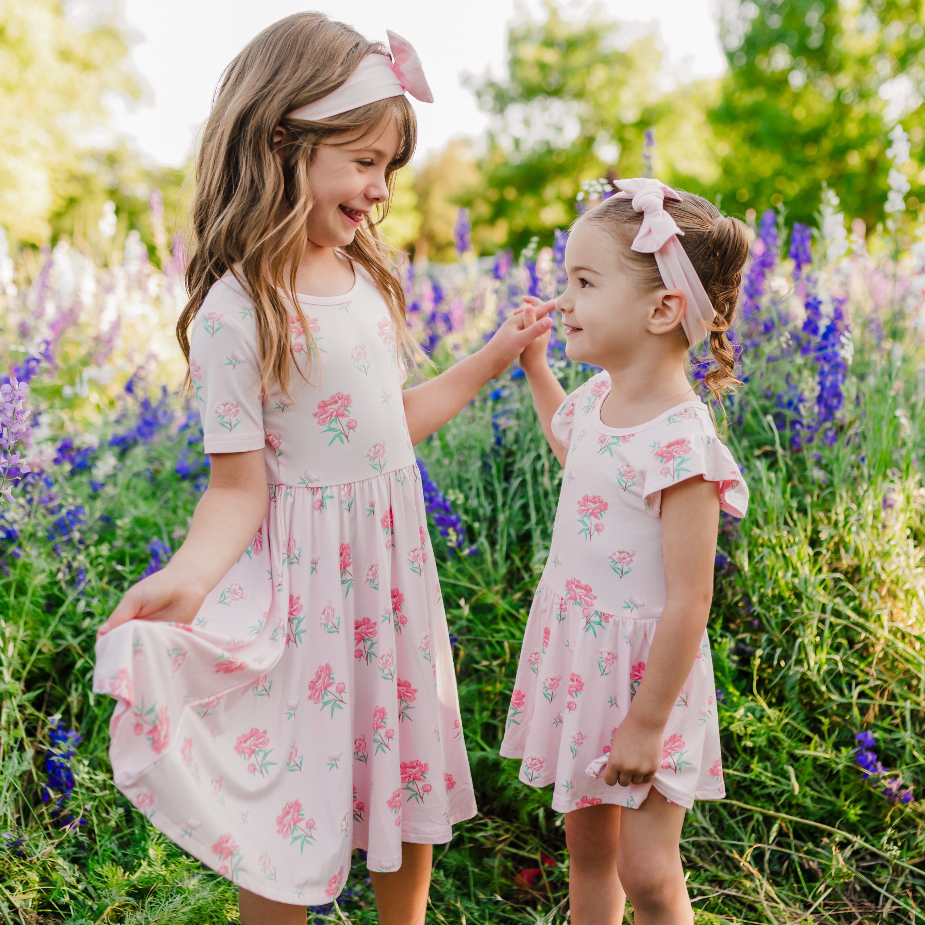 Child and toddler modeling Twirl Dress in Sakura Peony and Twirl Bodysuit Dress in Sakura Peony with a wildflower field in background