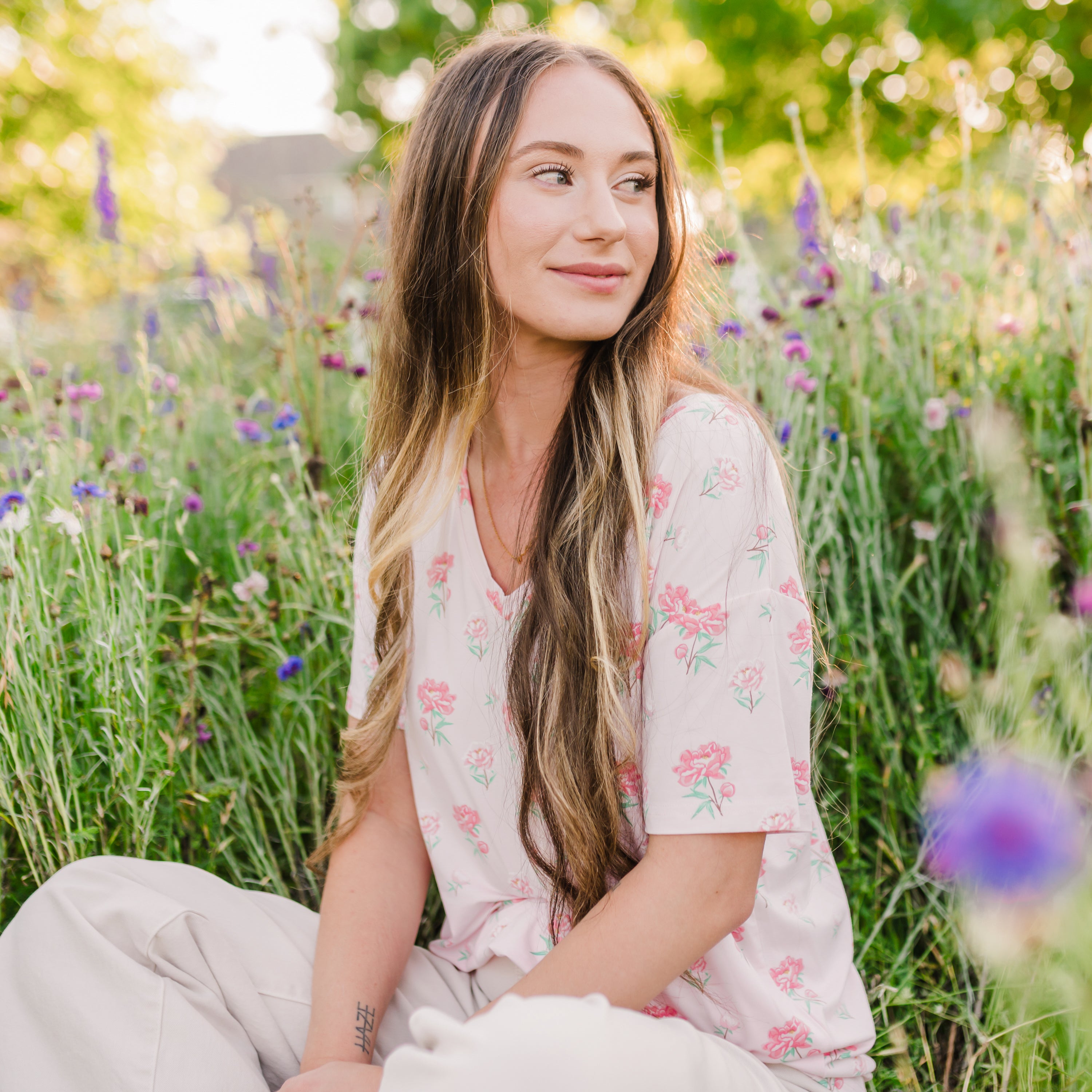 Woman sitting in a wildflower field wearing Women's Relaxed Fit V-Neck in Sakura Peony