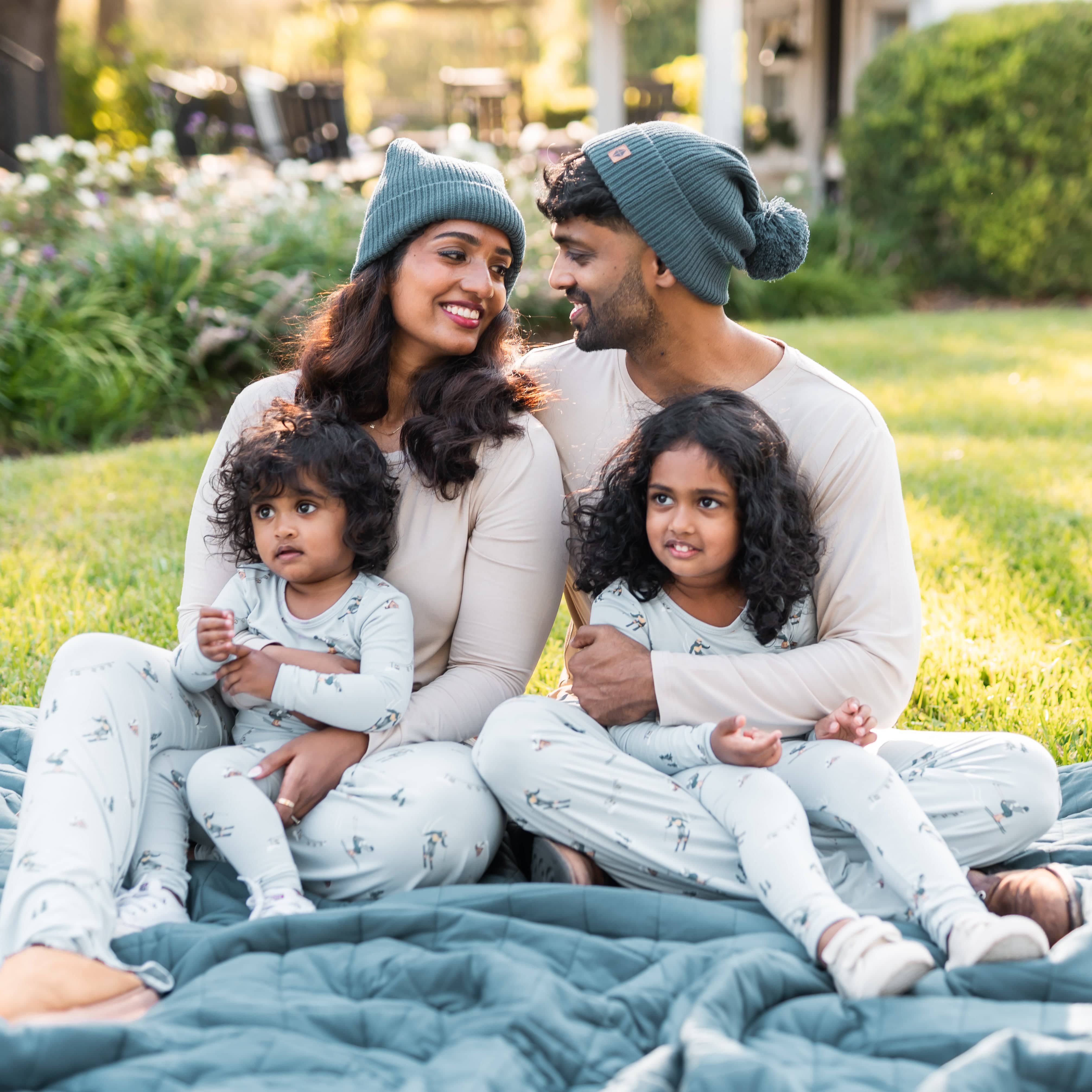 Family of four sitting on the grass on top of a blue blanket all matching in various items from the Ski collection