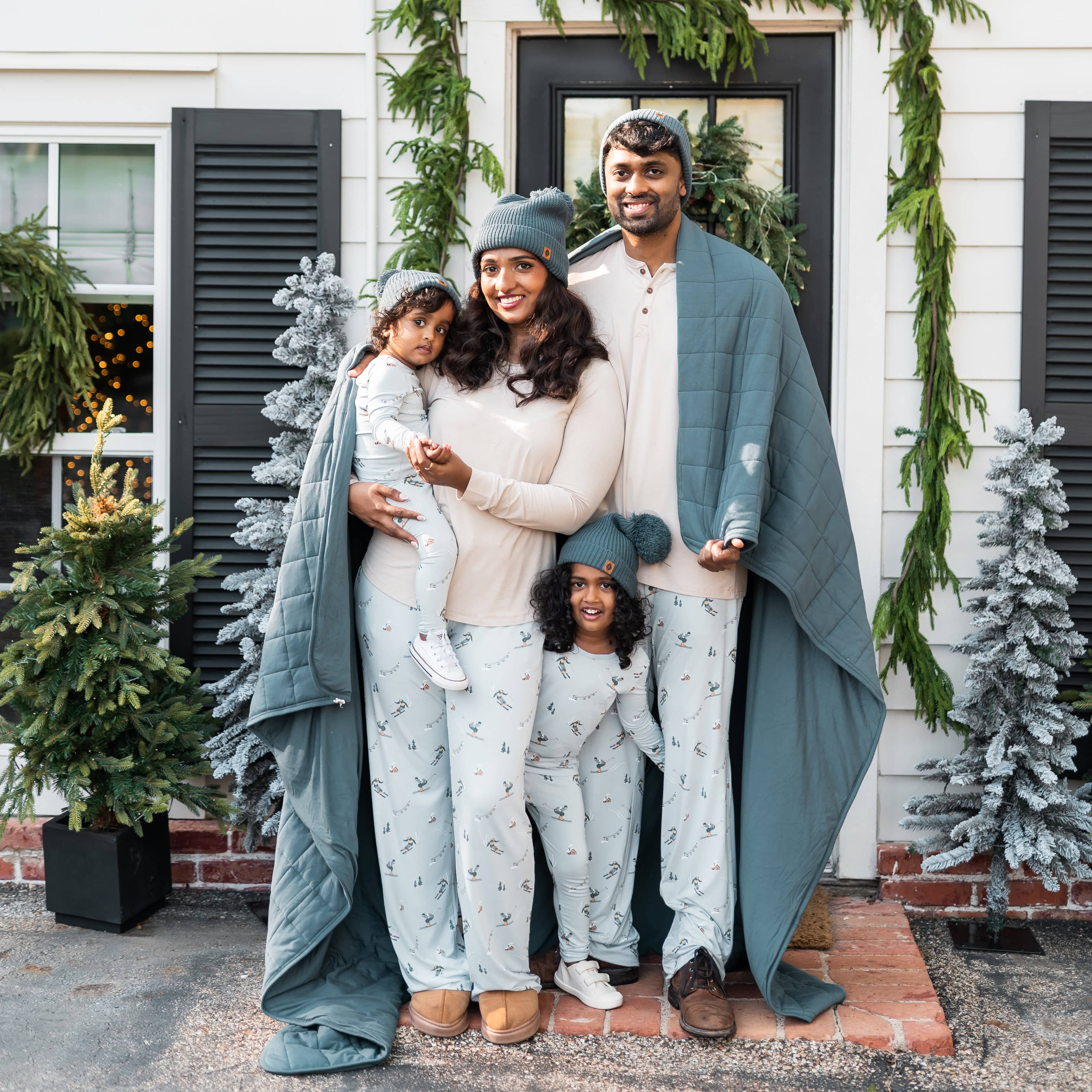 Family of four matching in various ski items standing at the front door of a house with an Atlantic blanket draped over the shoulder of the parents