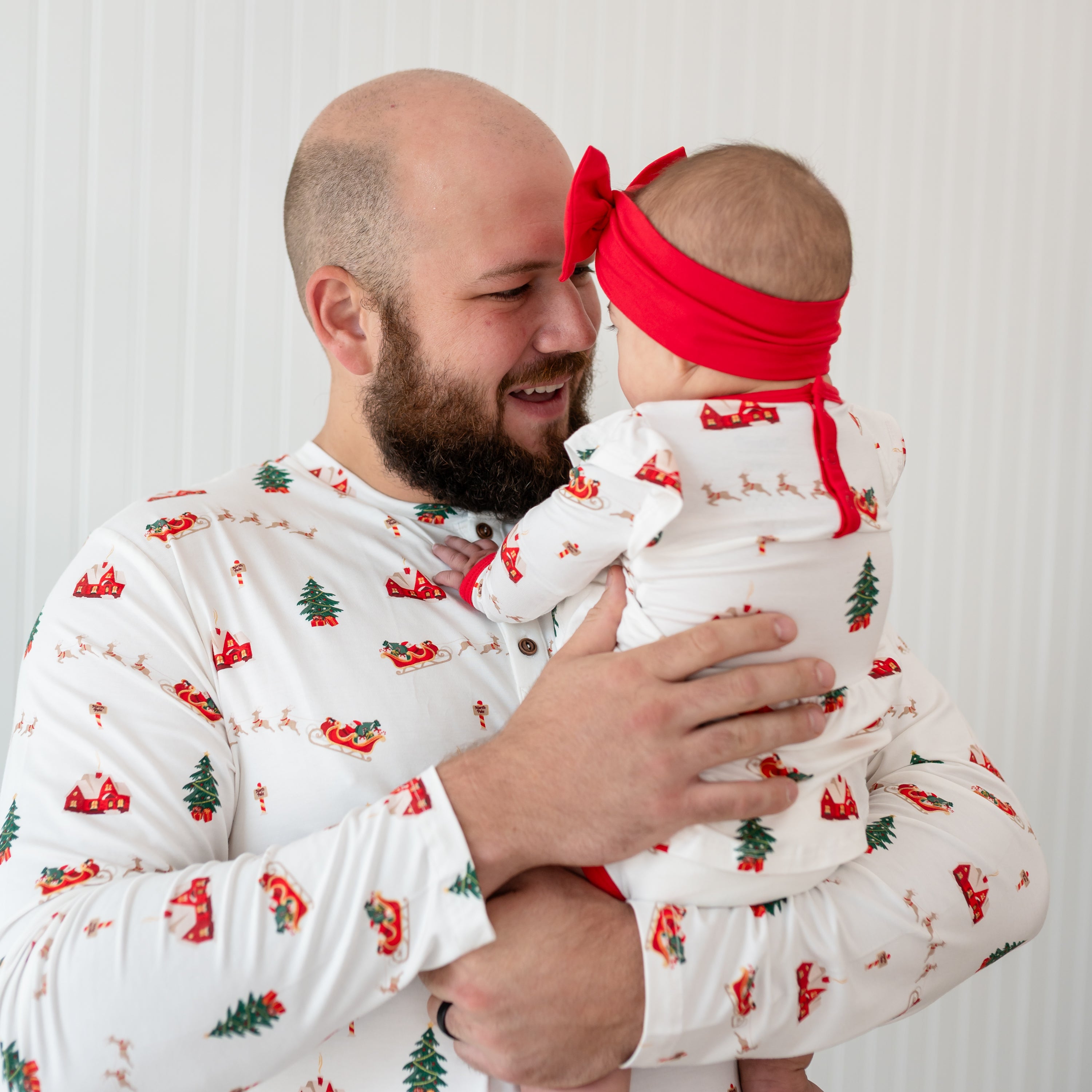 Father wearing the Men's Long Sleeve Henley Top in Santa Sleigh holding is daughter who is matching him in a long sleeve twirl bodysuit dress