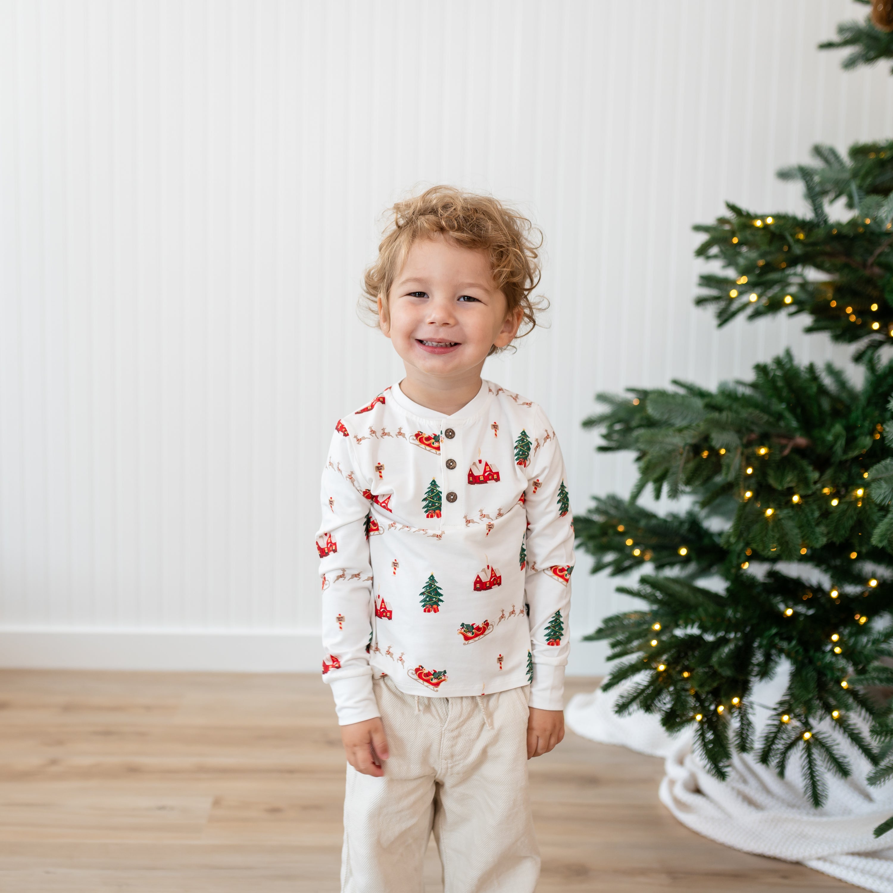 Close up of a young model wearing the Long Sleeve Toddler Henley Tee in Santa Sleigh with cream colored pants