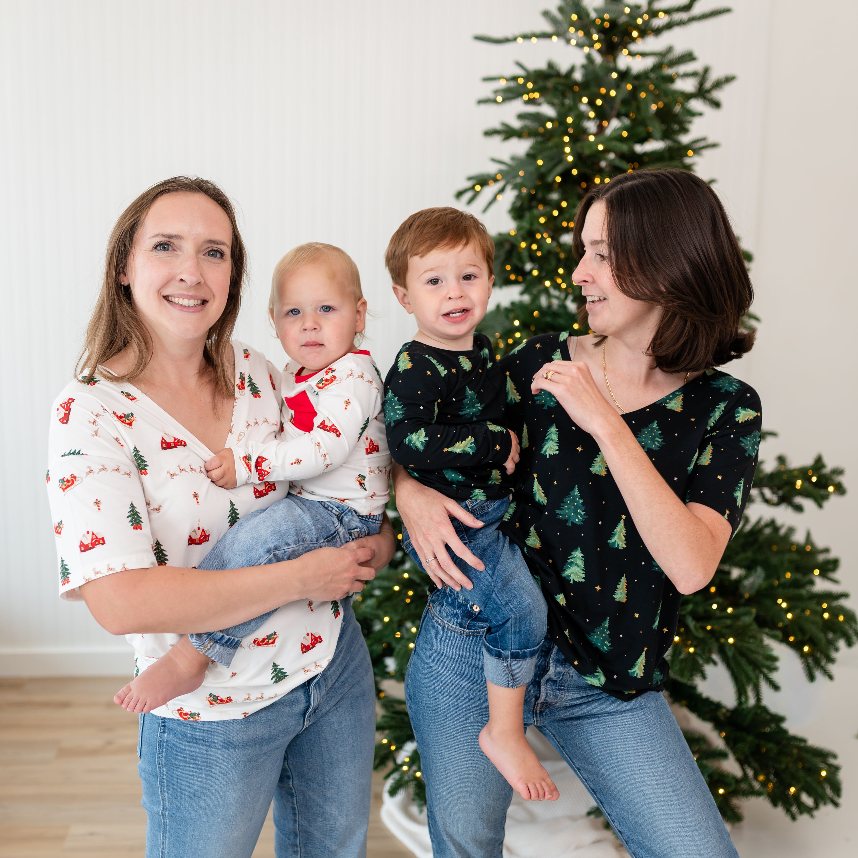 Two mothers holding their children both matching in Santa Sleigh and Twinkle Tree