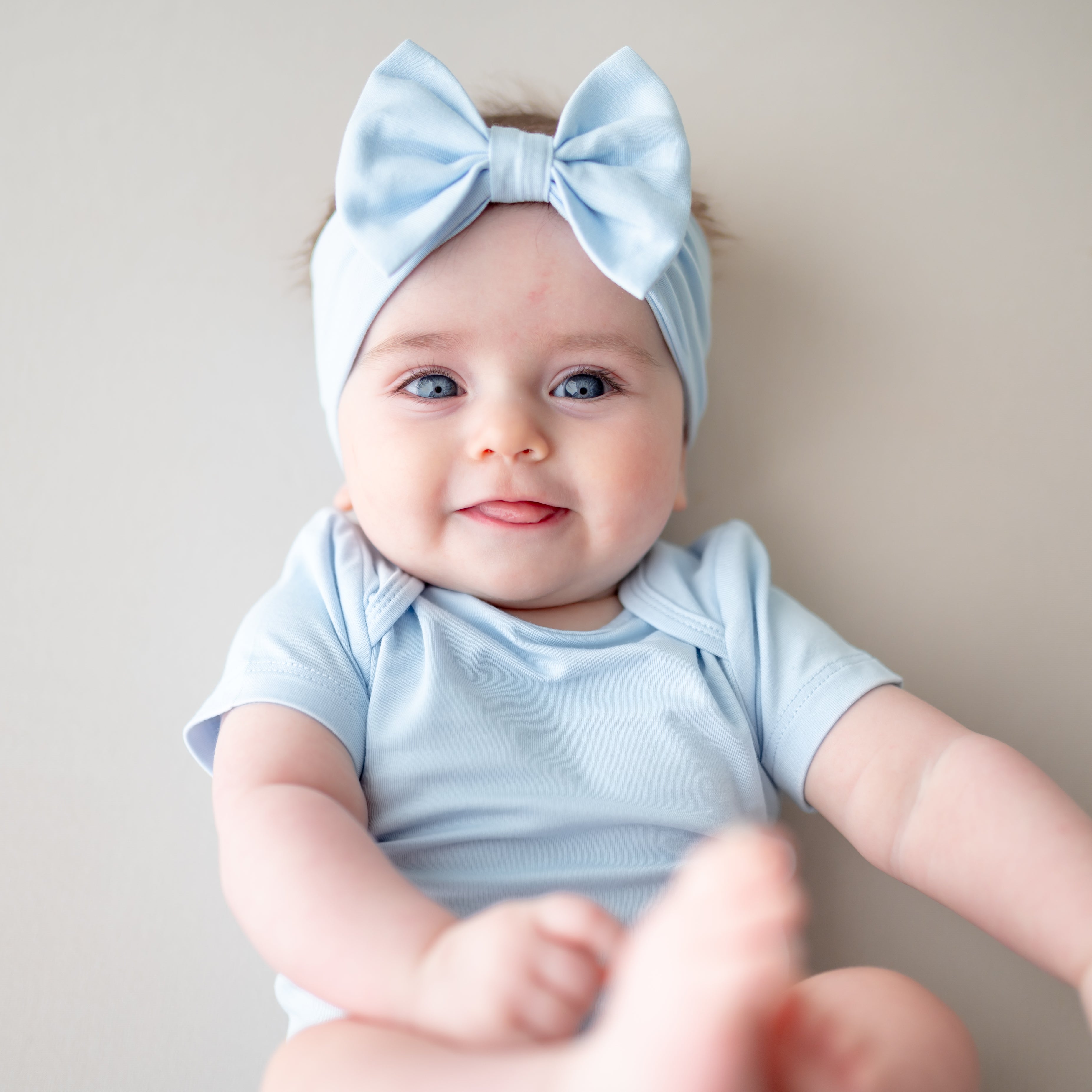 Baby wearing a light blue headband and onesie, sitting against a neutral background