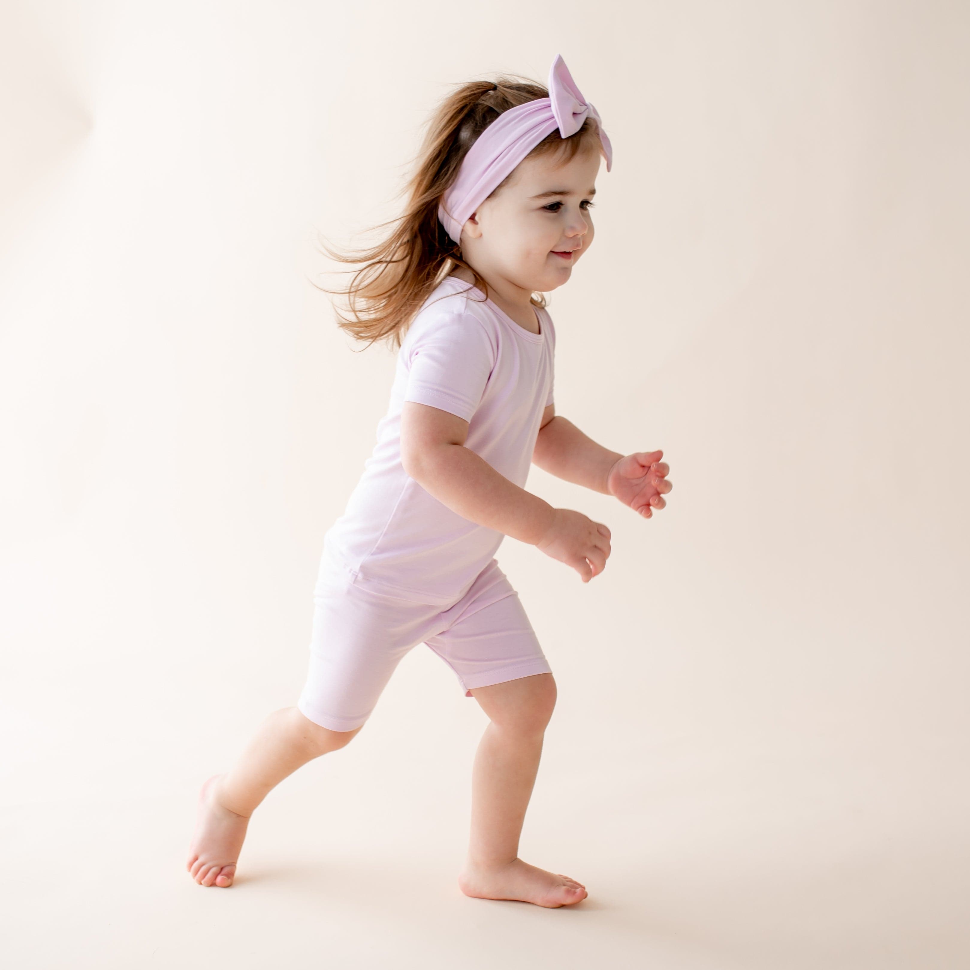 Child wearing a light purple outfit and headband on a plain background