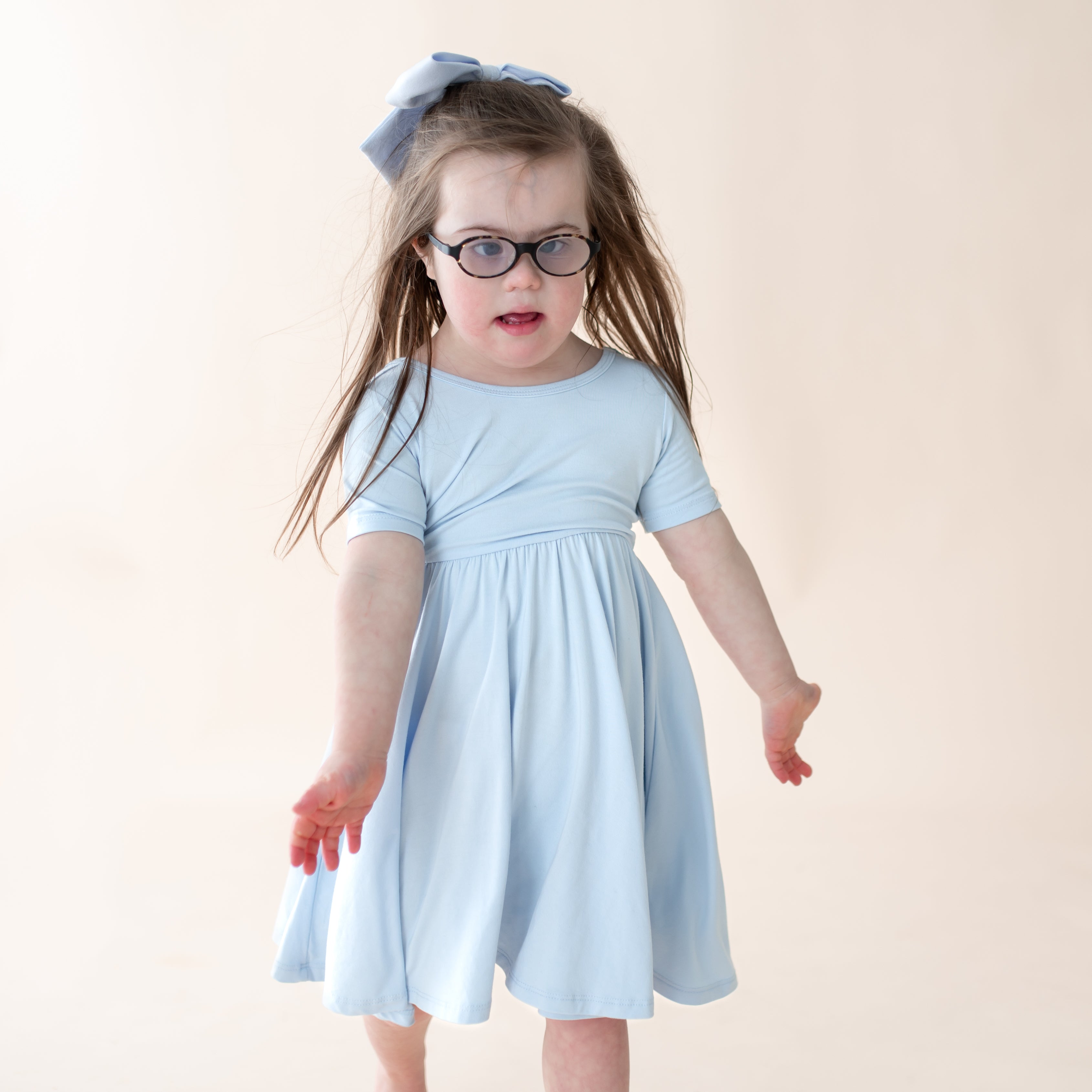 Child wearing a light blue dress and glasses on a plain background