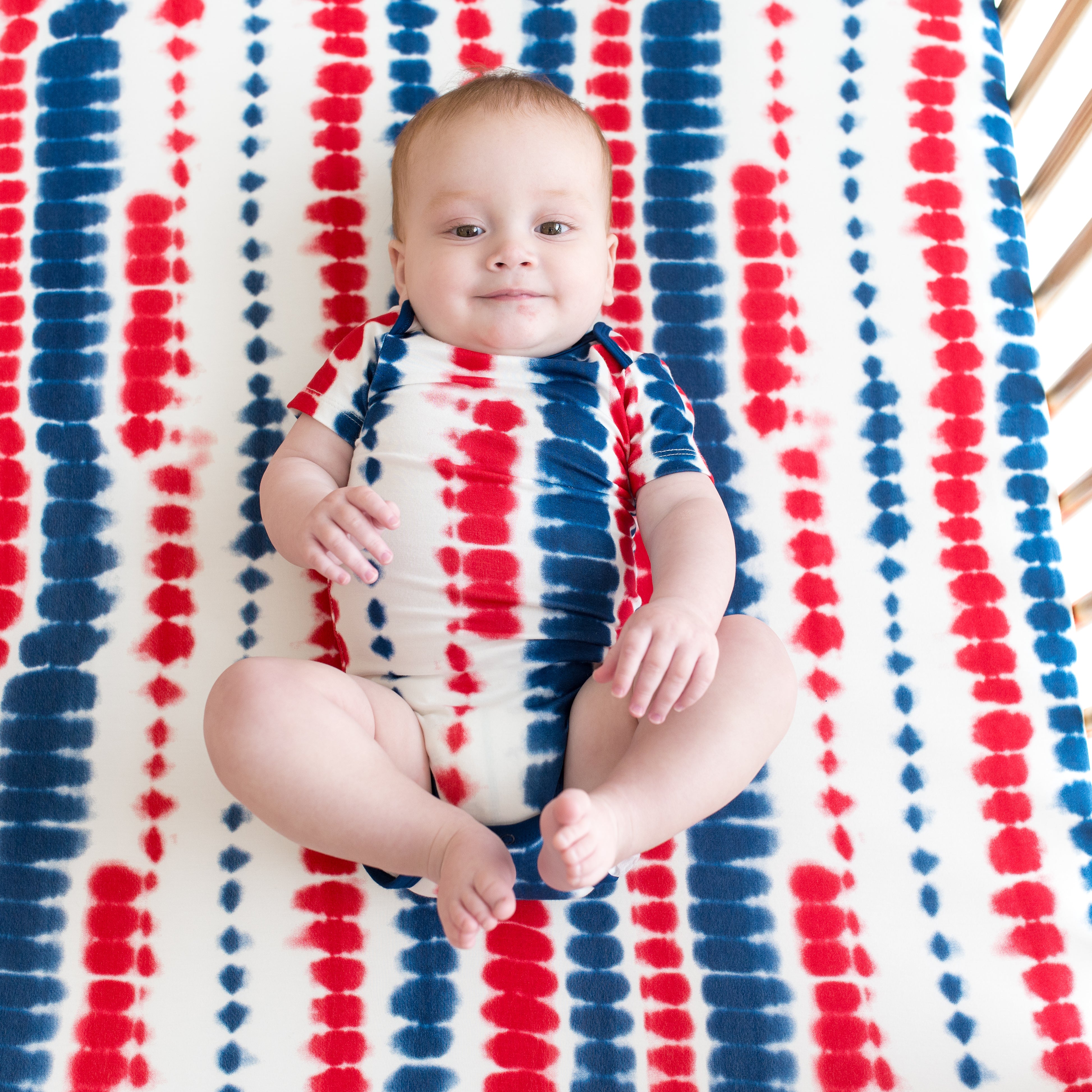 Baby modeling Bodysuit in Liberty Rip Tide on a Rip Tide crib sheet
