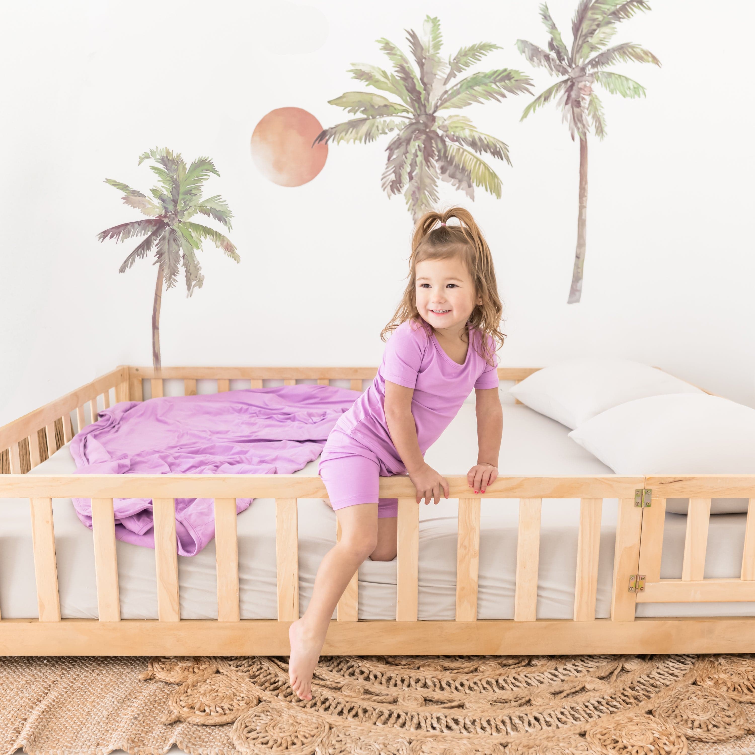 Toddler wearing Short Sleeve Kids Pajamas with matching Poi purple blanket on bed