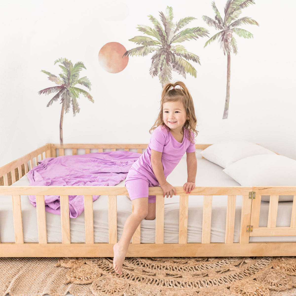Toddler wearing Short Sleeve Kids Pajamas with matching Poi purple blanket on bed