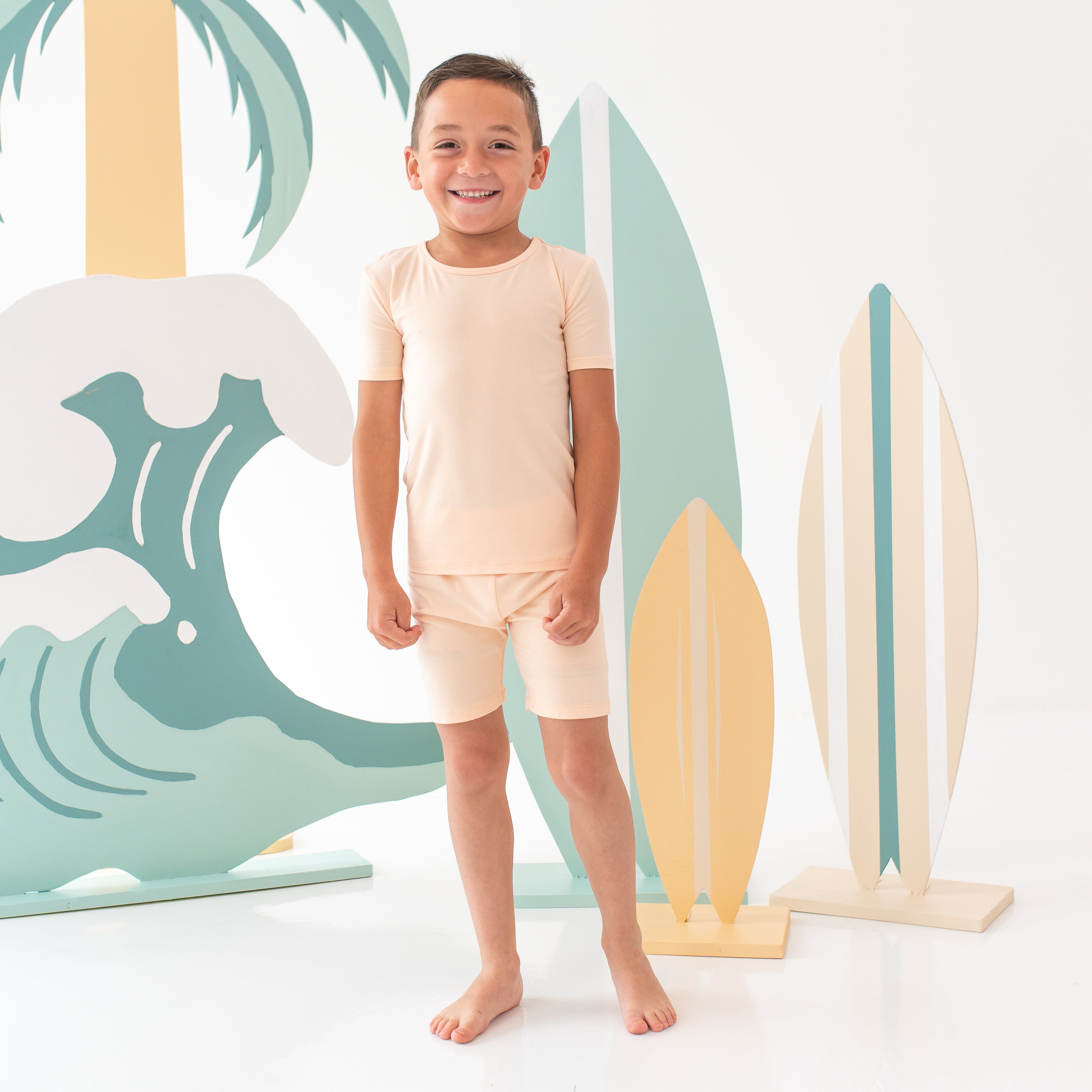 Smiling boy model wearing the Short Sleeve Pajamas in Canyon with surf boards as back drop