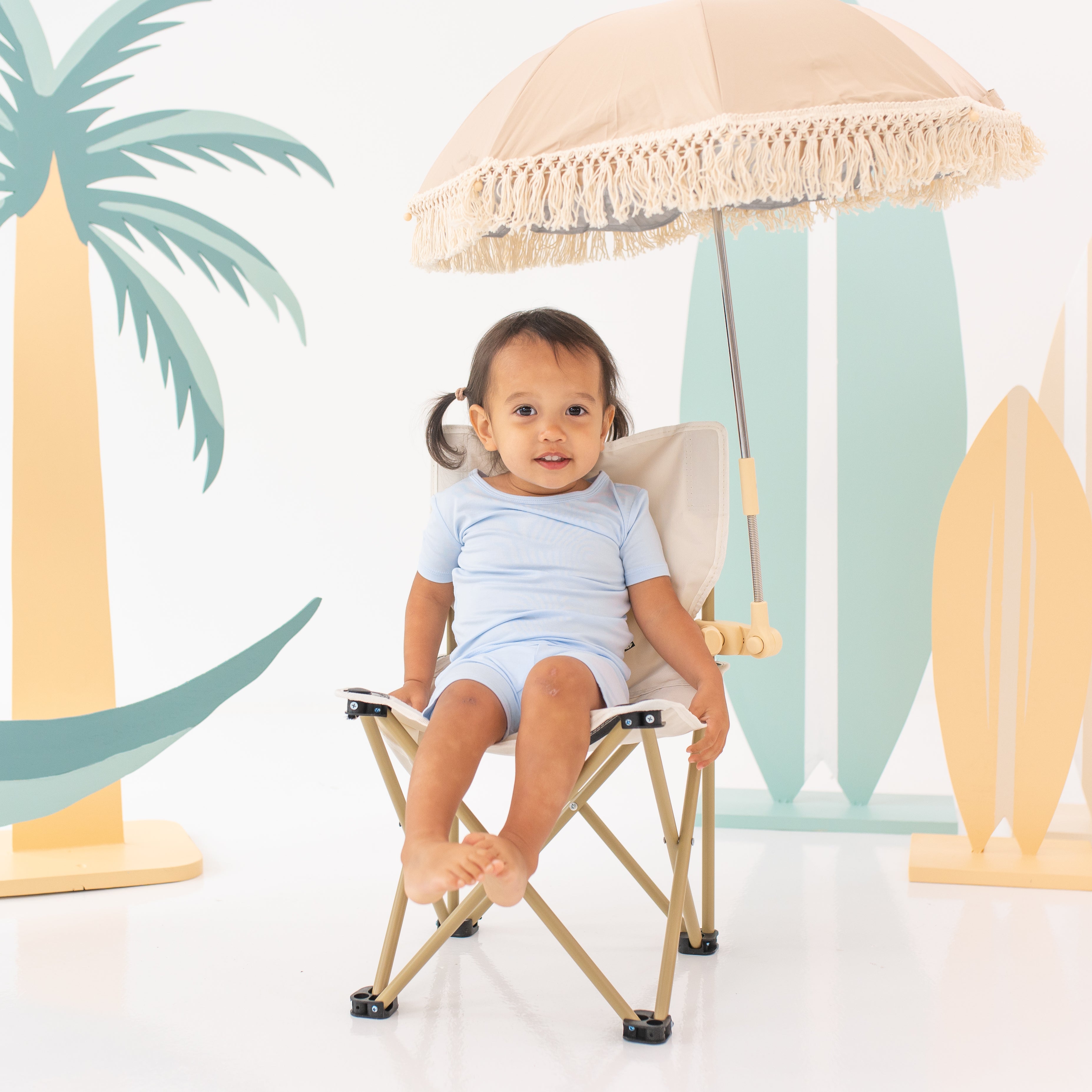 Toddler girl in pig tails sitting in a camping chair with an umbrella attached wearing the Short Sleeve Pajamas in Mist