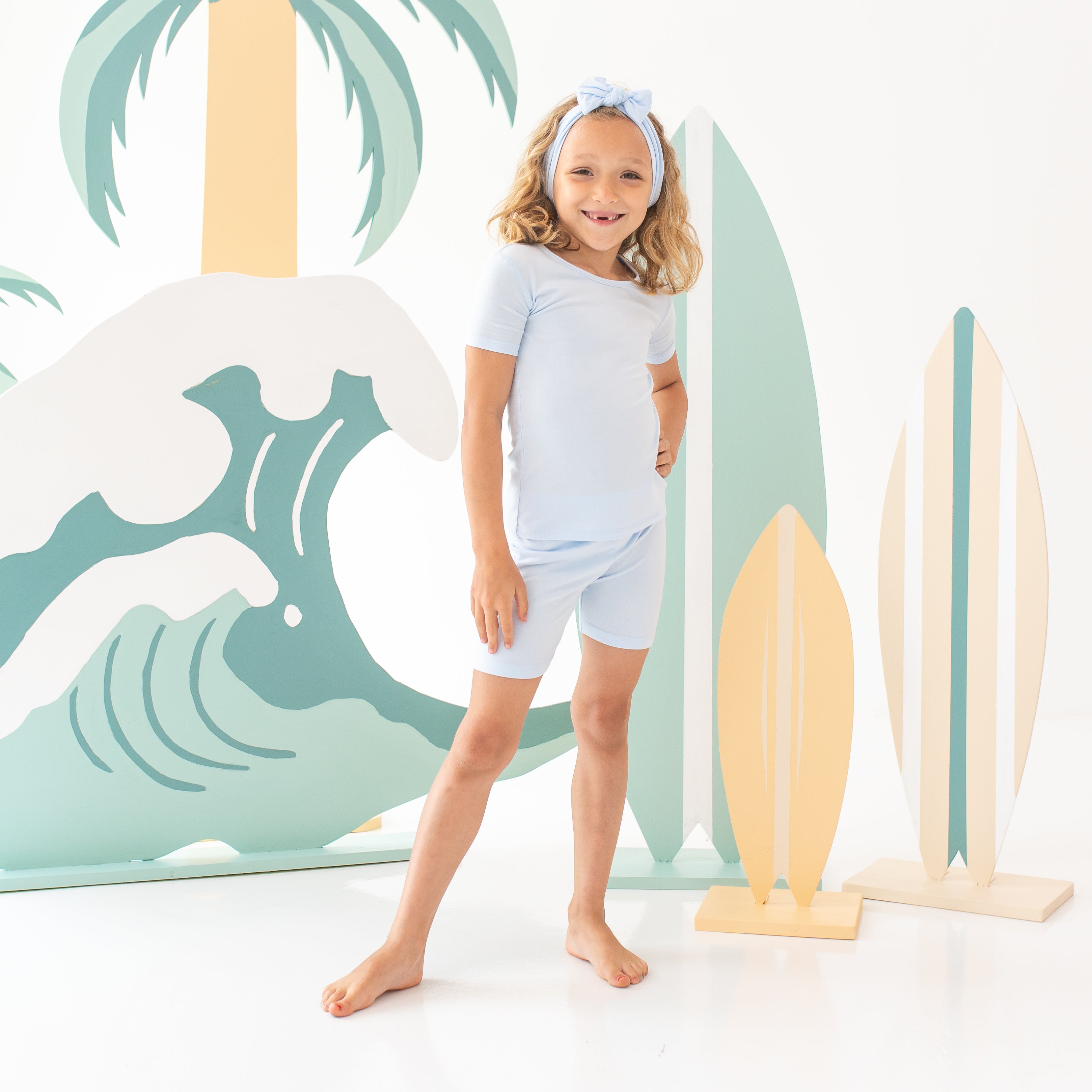 Young girl model standing with one hand on hip wearing the Short Sleeve Pajamas in Mist with matching knotted bow