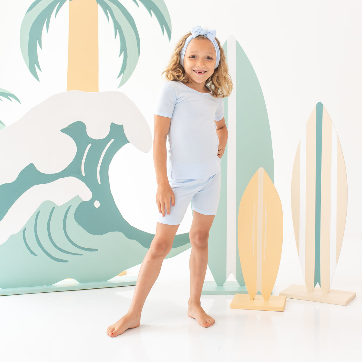 Young girl model standing with one hand on hip wearing the Short Sleeve Pajamas in Mist with matching knotted bow