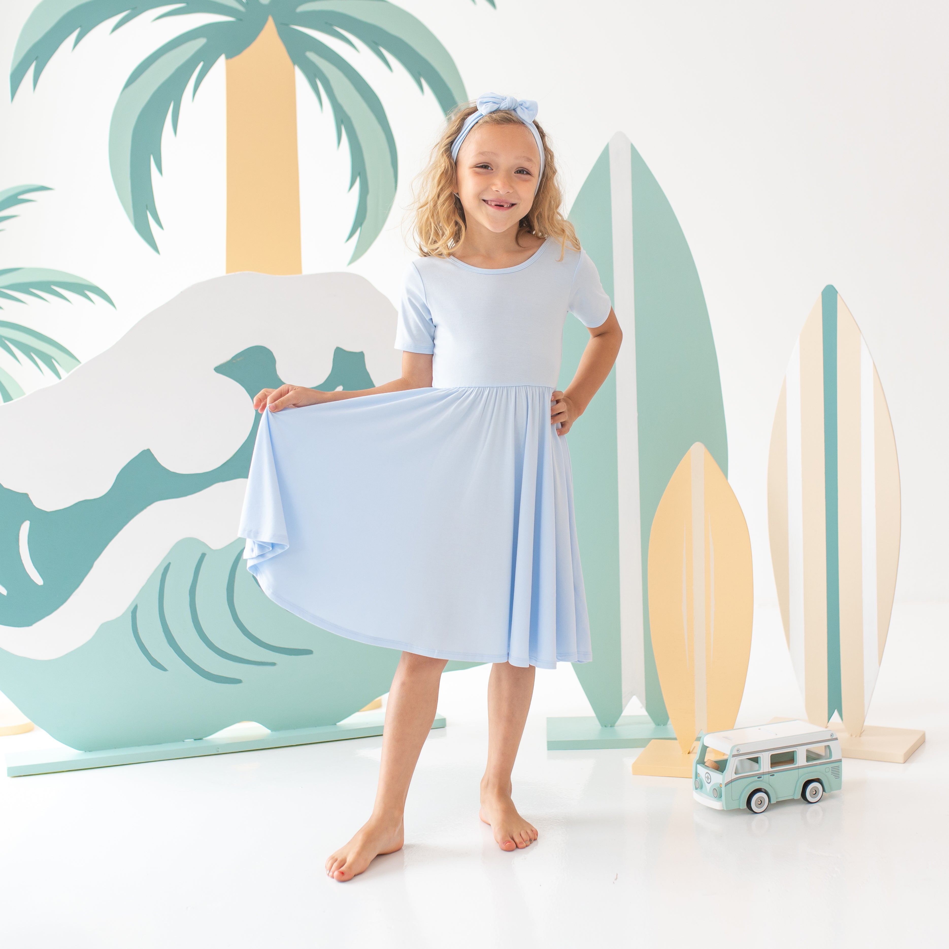 Young female model holding one side of the hem on the Twirl Dress in Mist up with her hand with the other hand on her hip