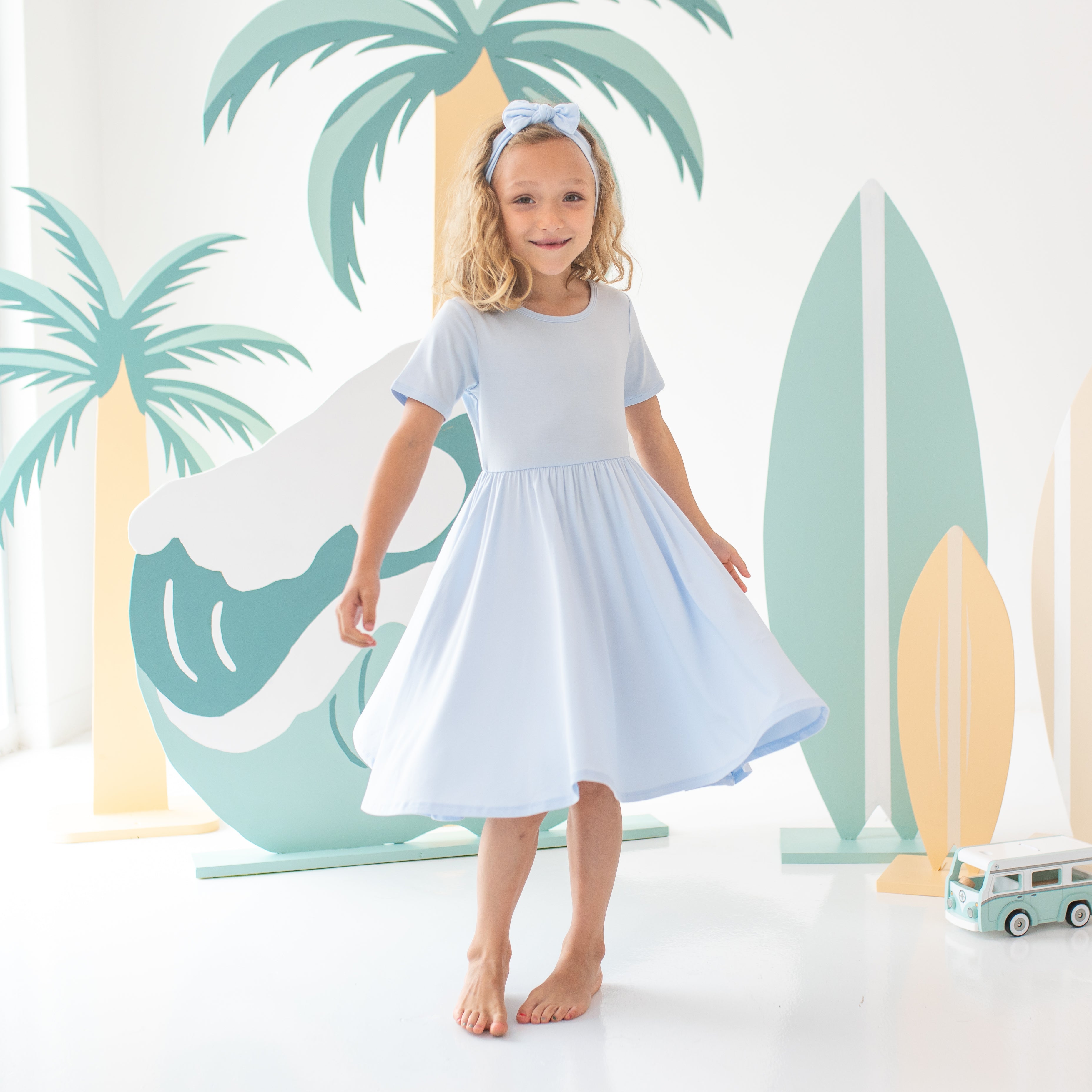 Young female model twirling in the Twirl Dress in Mist paired with a matching knotted bow