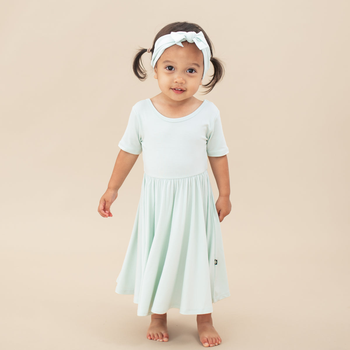 Young girl wearing the Twirl Dress in Dew with matching knotted bow