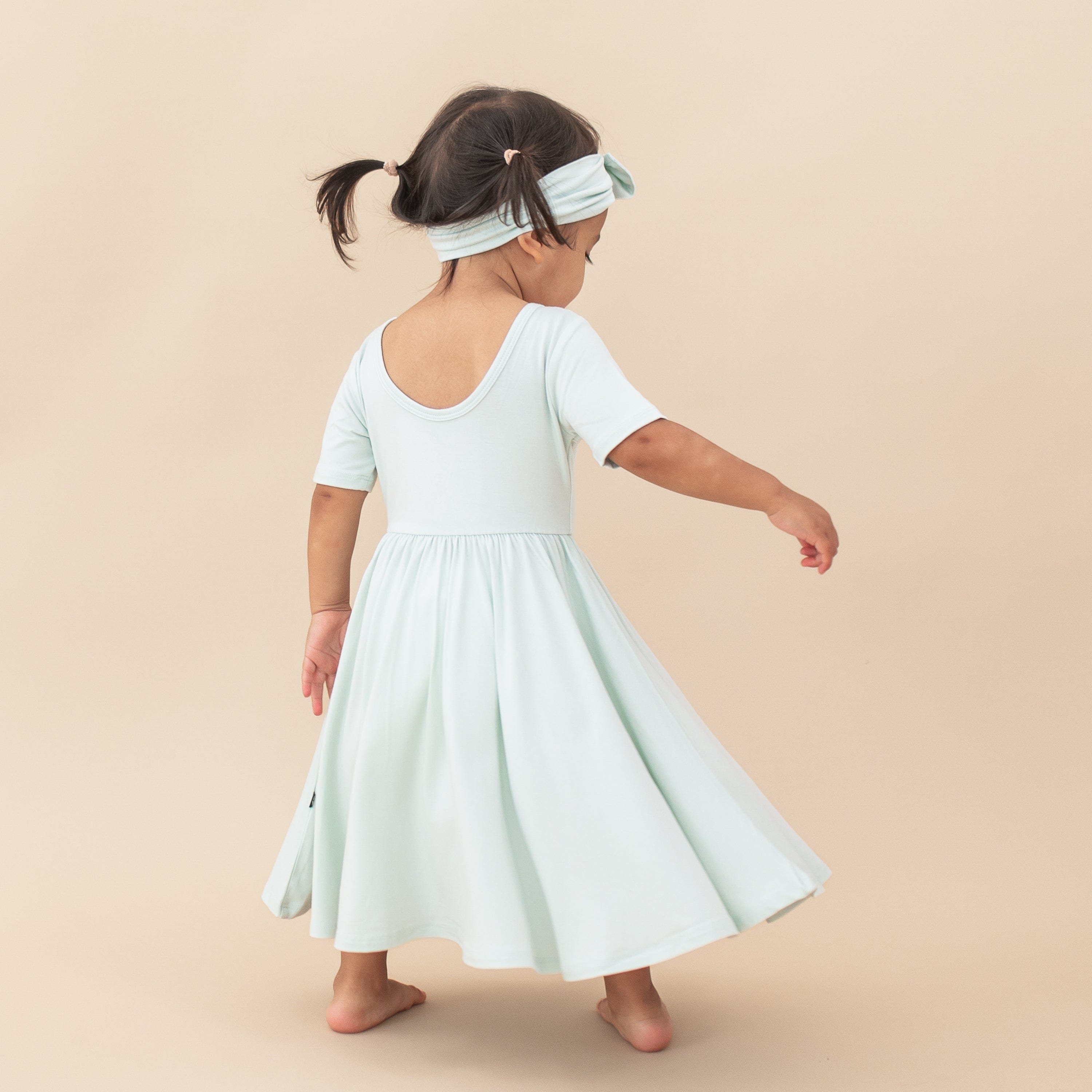 Young toddler girl twirling in the Twirl Dress in Dew