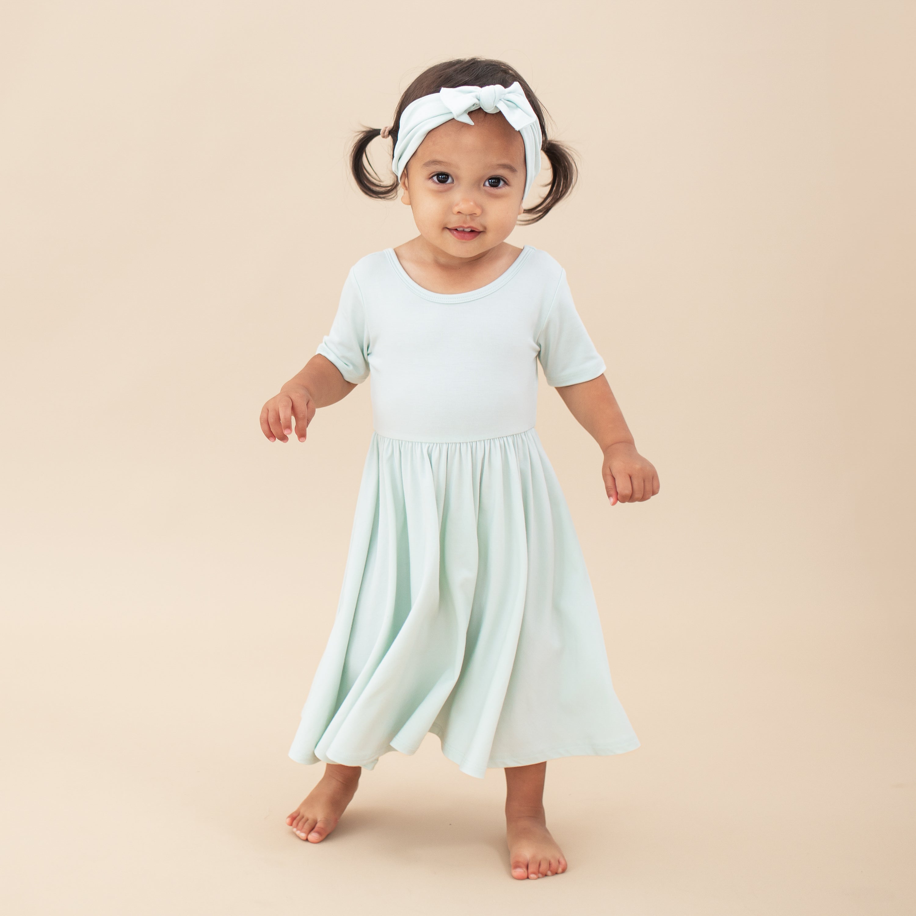 Young child model wearing the Knotted Bow Headband in Dew with a Dew Twirl Dress