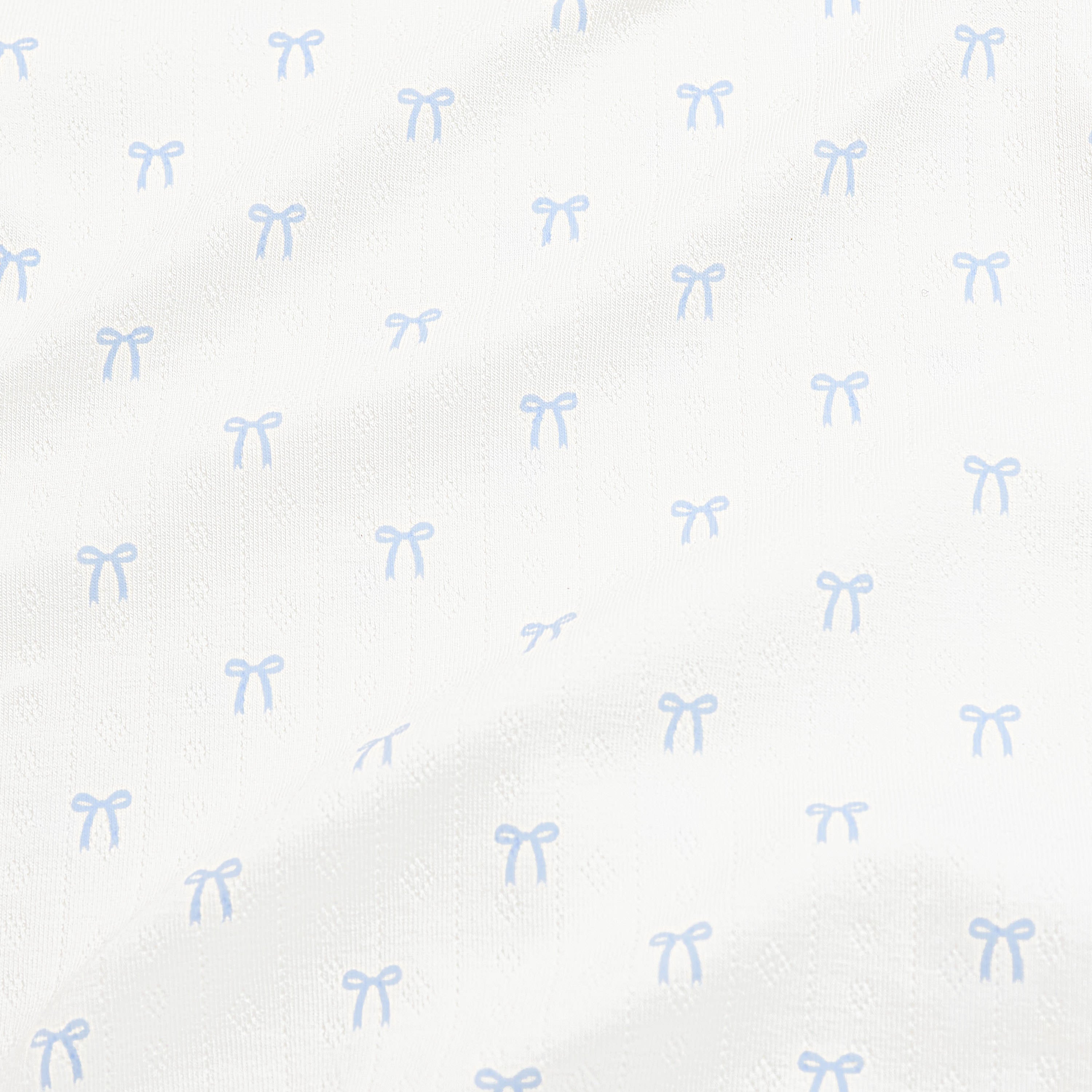Close up of the pointelle fabric: An all-over print of dainty light blue bows over a white background.