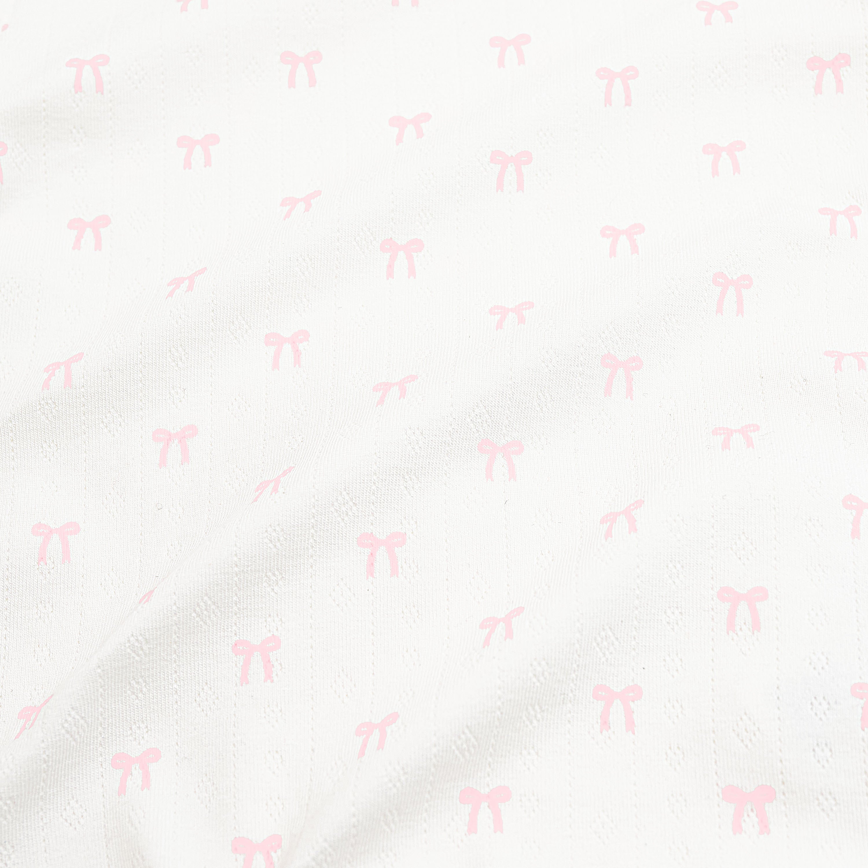 Close up of the pointelle fabric: An all-over print of dainty light pink bows over a white background.