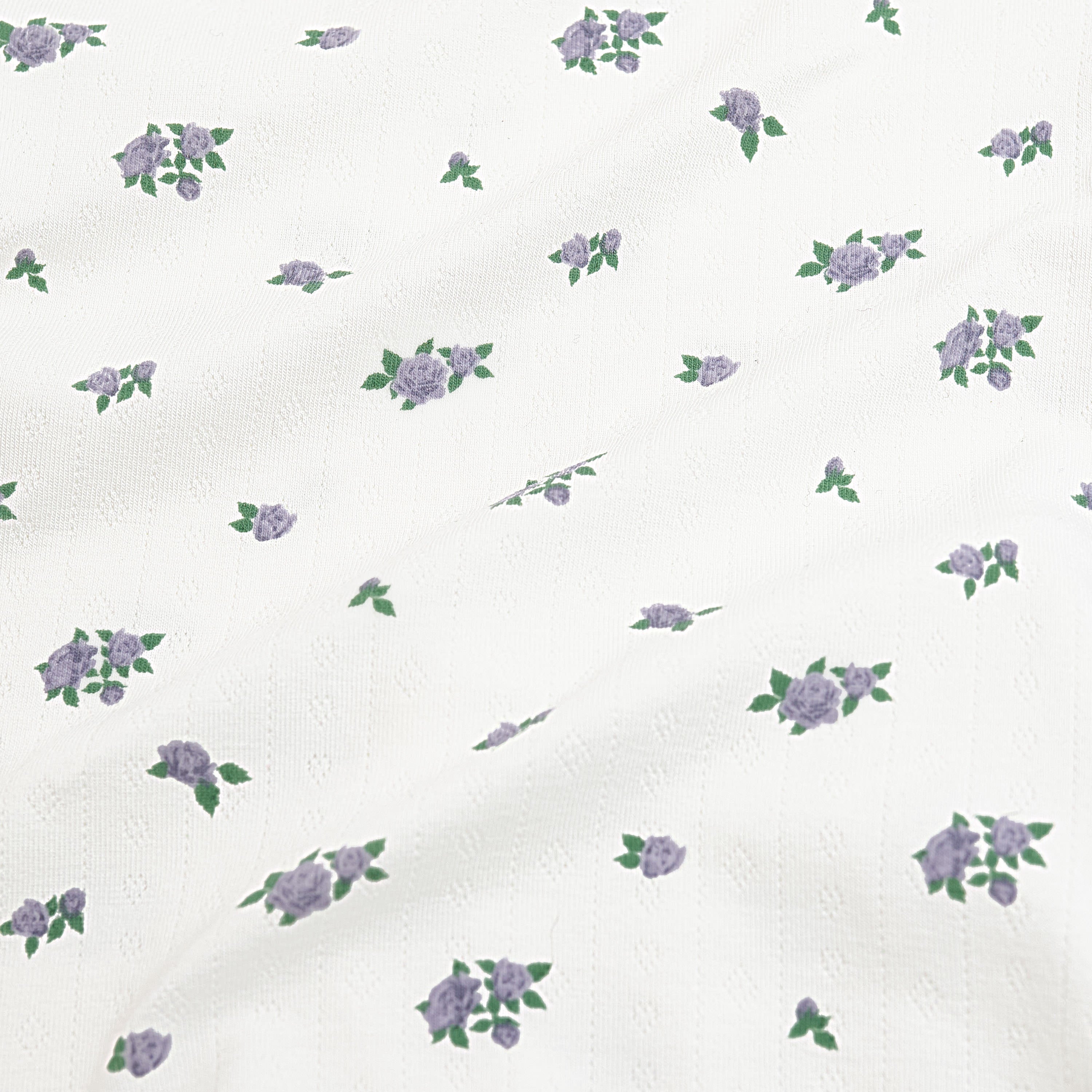 Close up of the pointelle fabric: An all-over print featuring clusters of three purple spray roses with green leaves over a white background.