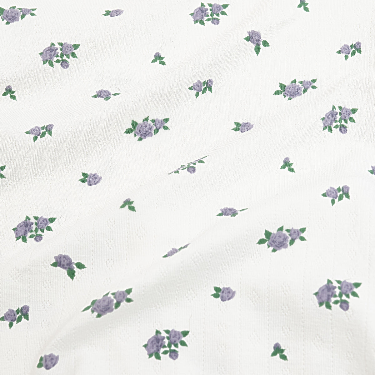 Close up of the pointelle fabric: An all-over print featuring clusters of three purple spray roses with green leaves over a white background.