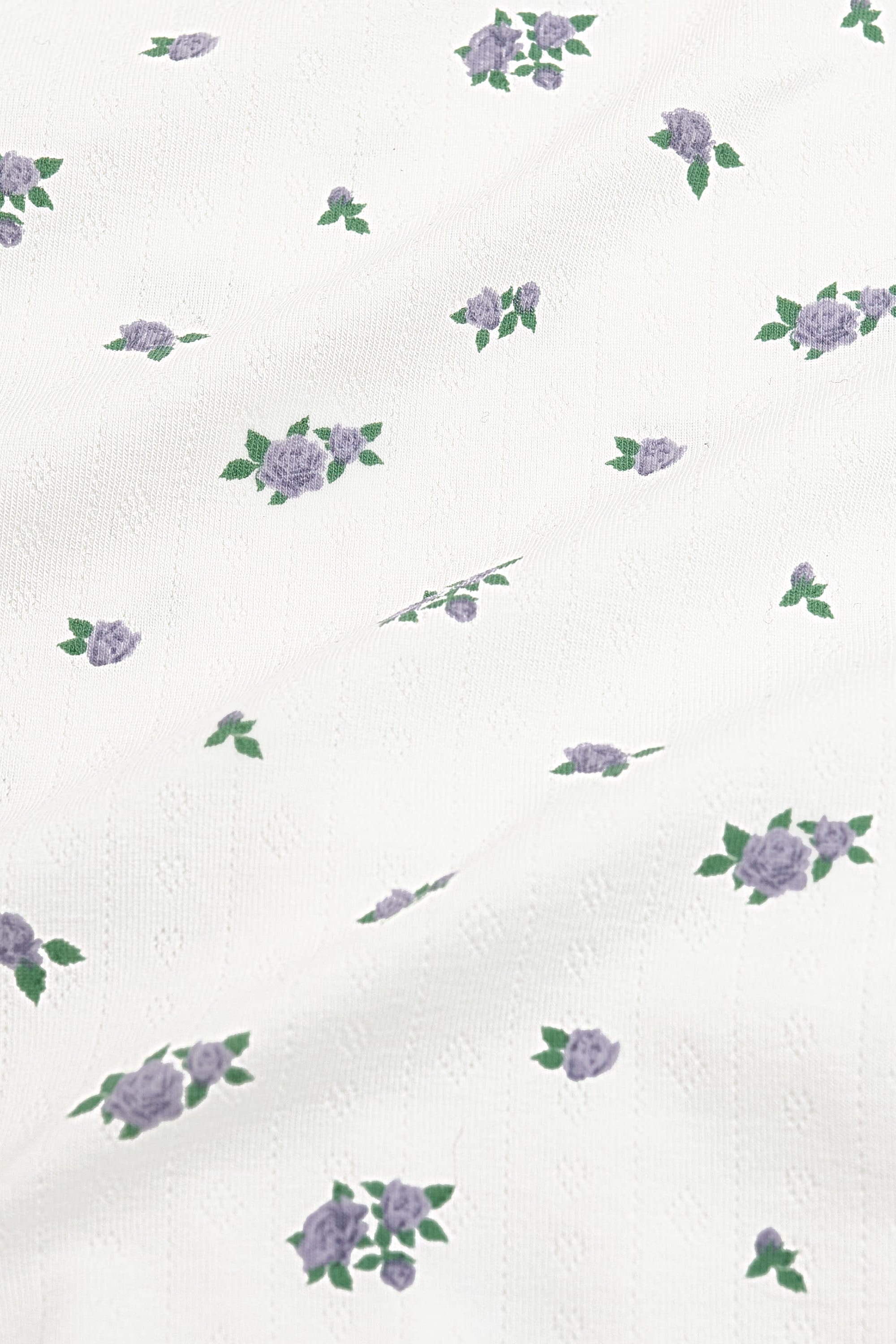Close up of the pointelle fabric: An all-over print featuring clusters of three purple spray roses with green leaves over a white background.