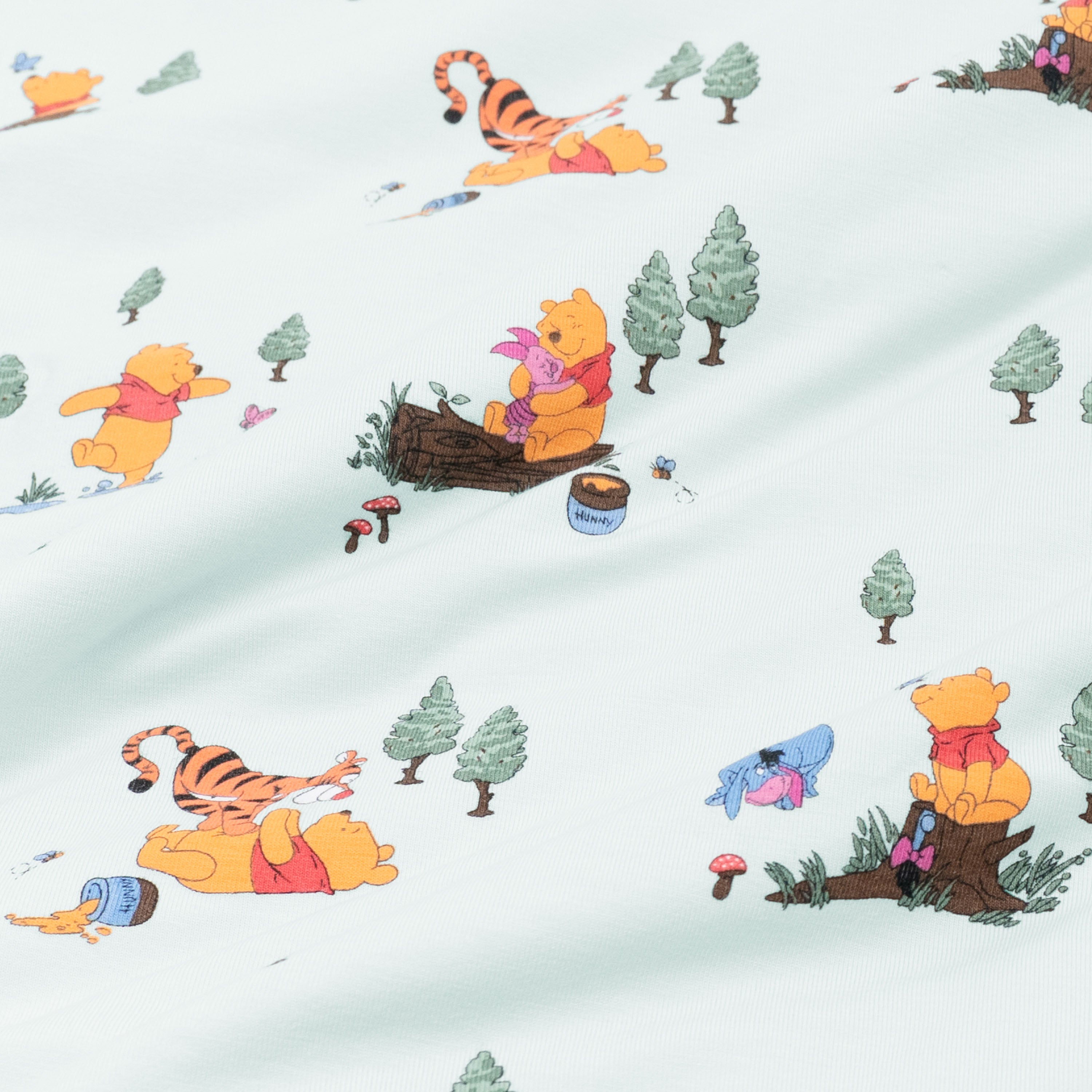 Close up of fabric swatch of the Winnie the Pooh Hundred Acre Wood showing the book characters on a light green background