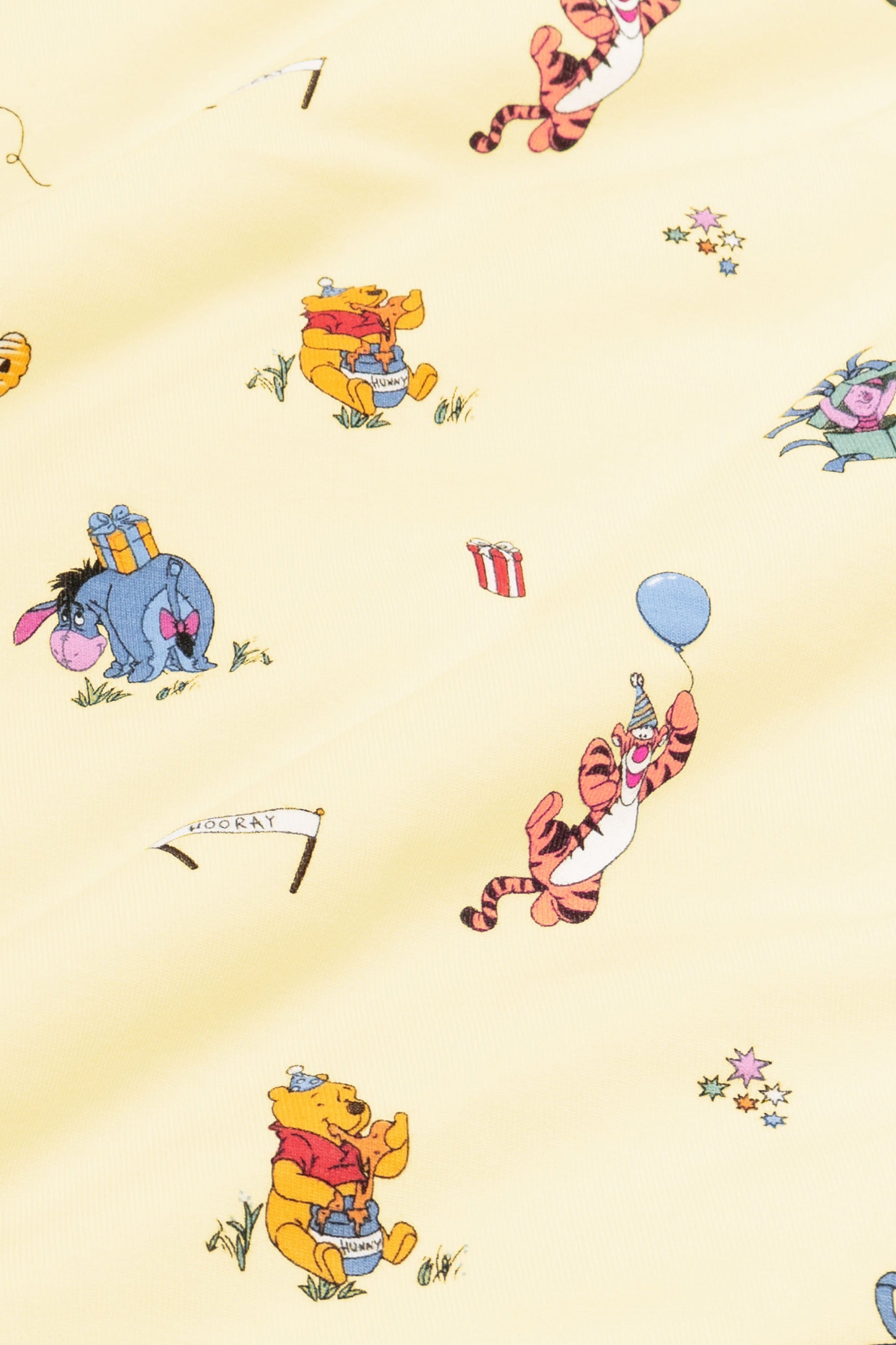 Close up of fabric swatch of the Winnie the Pooh Celebration print showing the story book characters on a yellow background