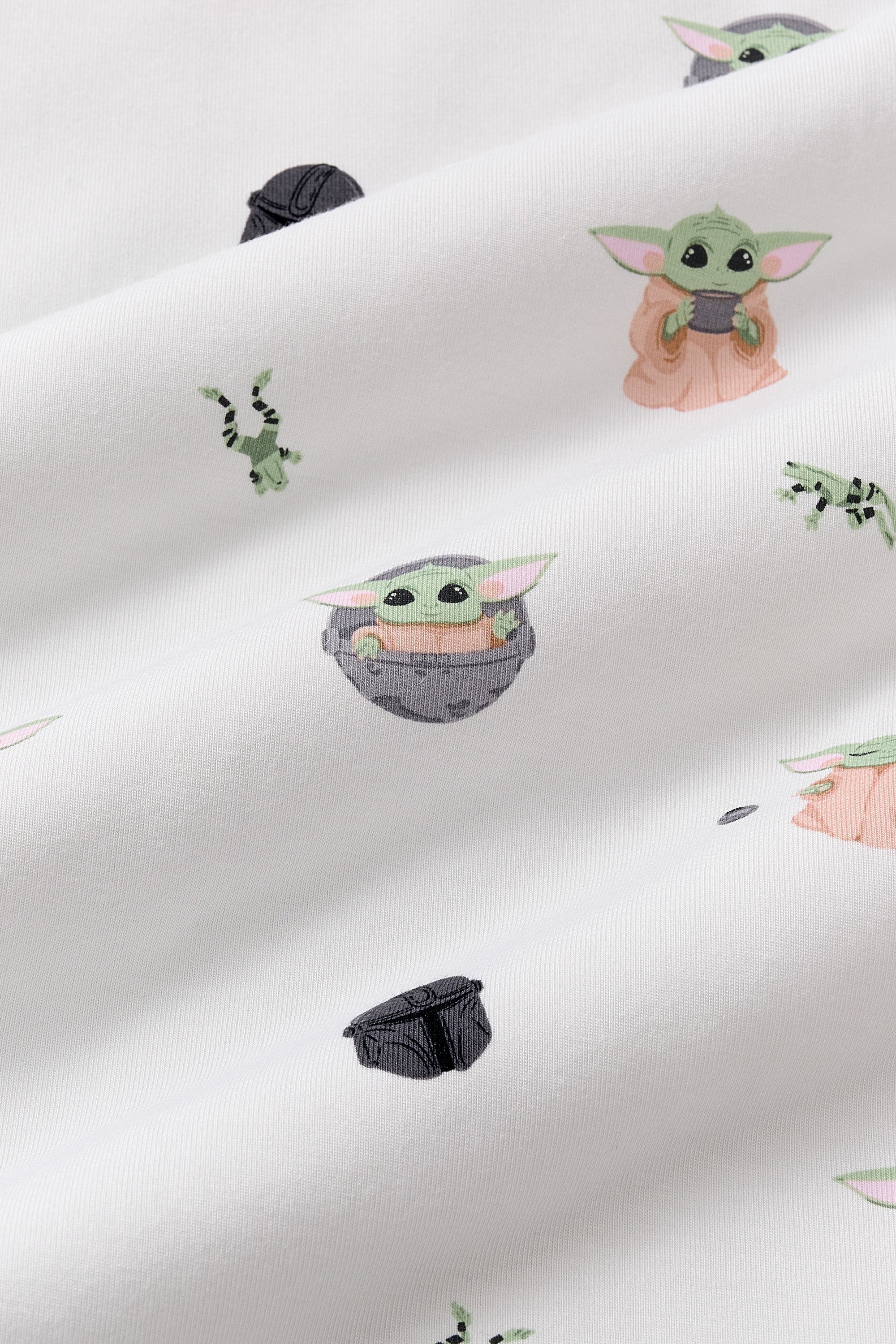 Close up of the bamboo fabric: A repeating, all-over print featuring Grogu in a hover pram; a dark grey Mandalorian helmet; Grogu holding a grey cup; Grogu with his eyes closed, telekinetically manipulating a small silver ball; and leaping green Arges Frogs with black stripes, over a white background.